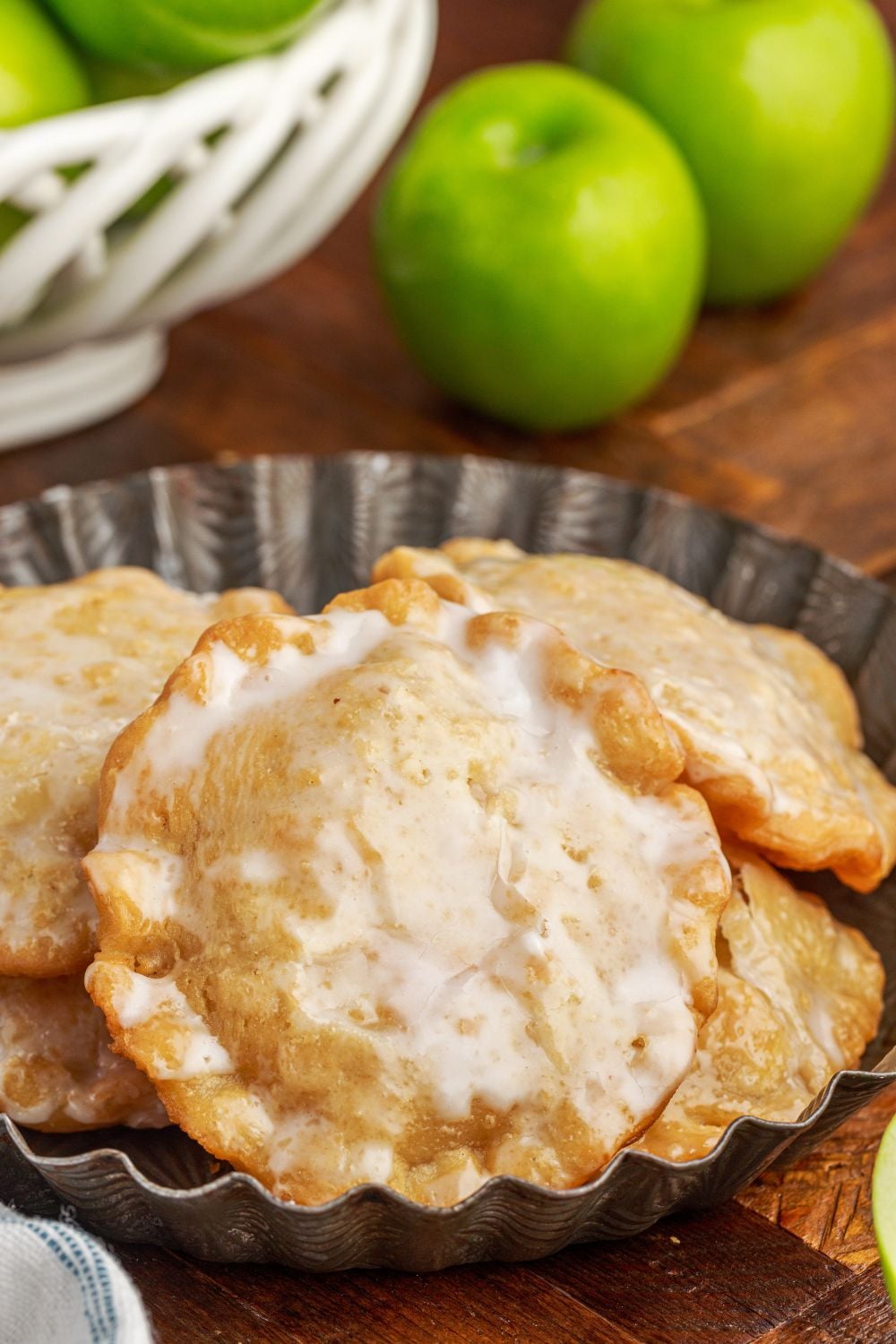 Deep Fried Apple Hand Pies on a plate with a bowl of apples to the side to show glazed hand pies