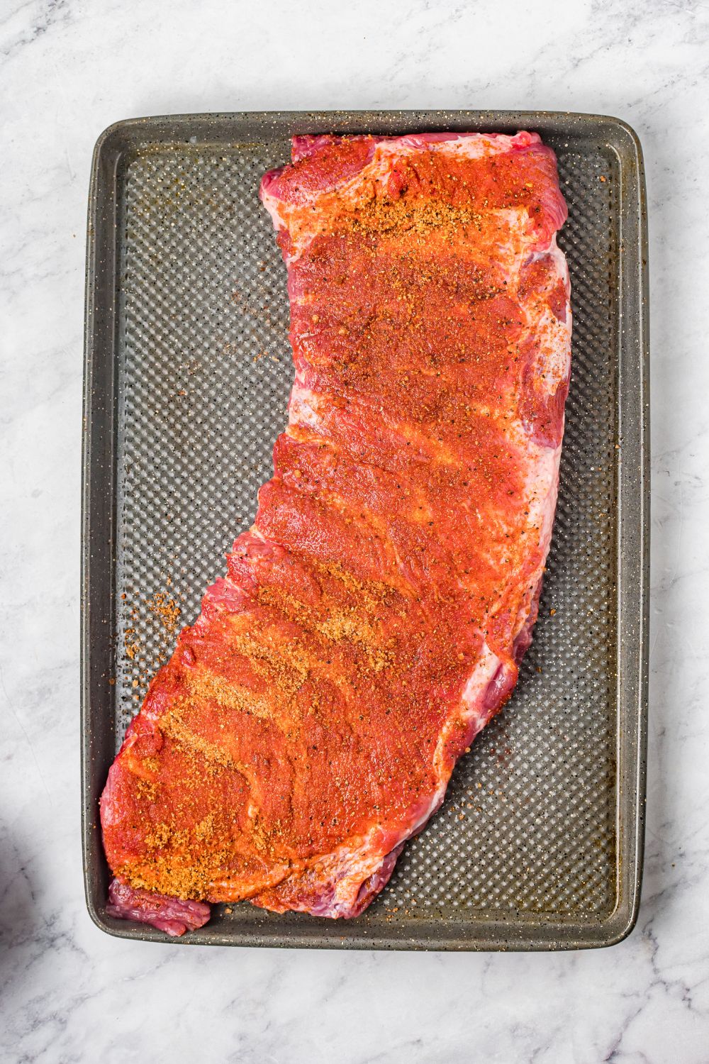 raw BBQ Baby Back Rib on baking sheet covered in bbq rub