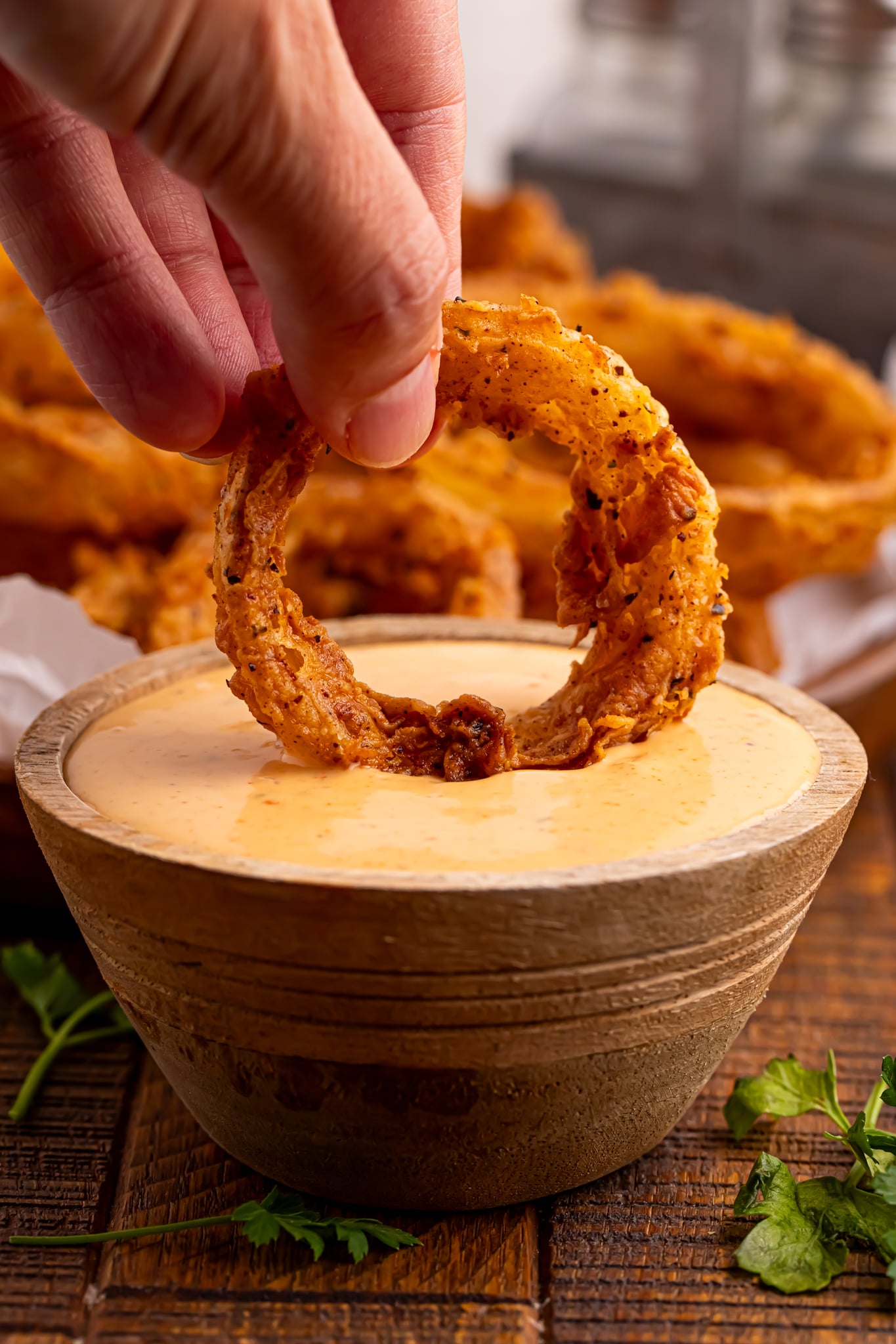 a Hand dipping a onion ring in sauce