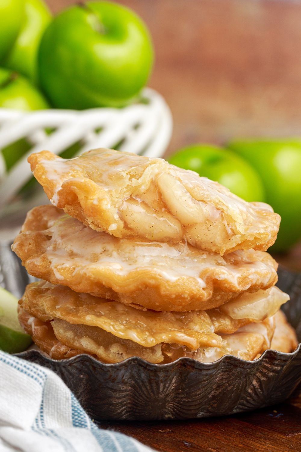 Deep Fried Apple Hand Pies stacked on table with apples in a bowl and apples to side