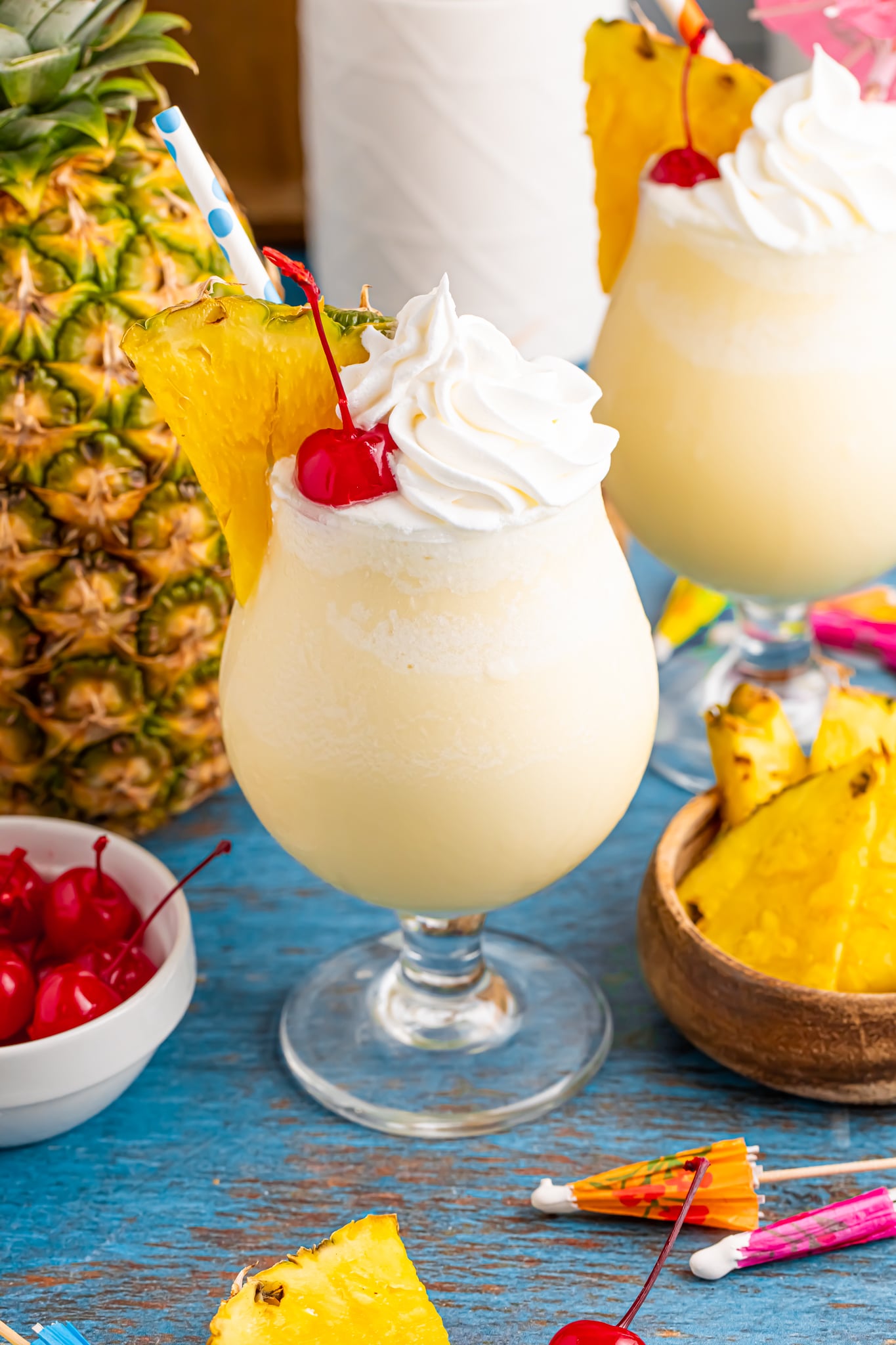 Frozen Malibu Piña Colada in a cocktail glass with a whole pineapple to side, bowl of cherries and pineapples 