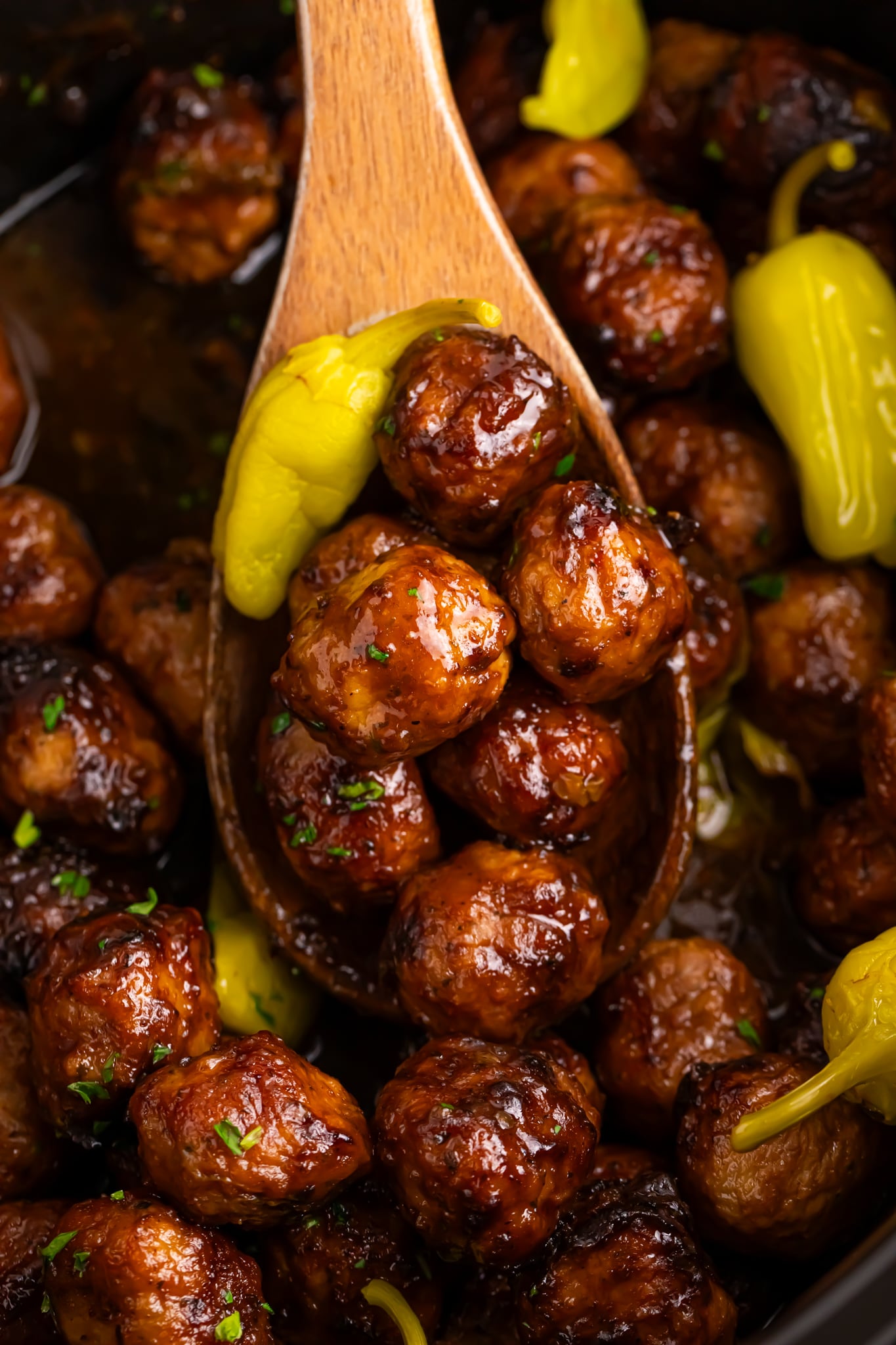 wooden spoon being held above Crockpot with Mississippi meatballs in it
