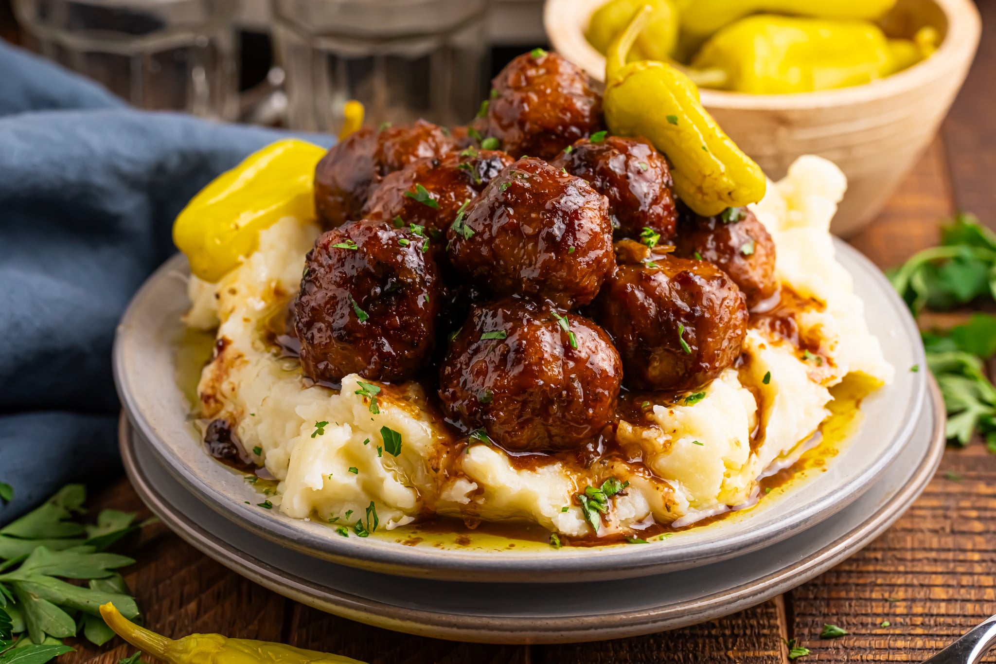 Crockpot Mississippi Meatballs on a stack of plates with more peppers over mashed potatoes