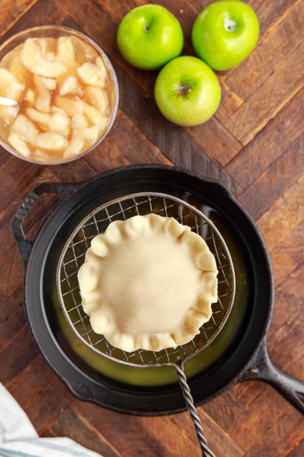 Deep Fried Apple Hand Pie in a ladle above pot with hot oil and apples to the side