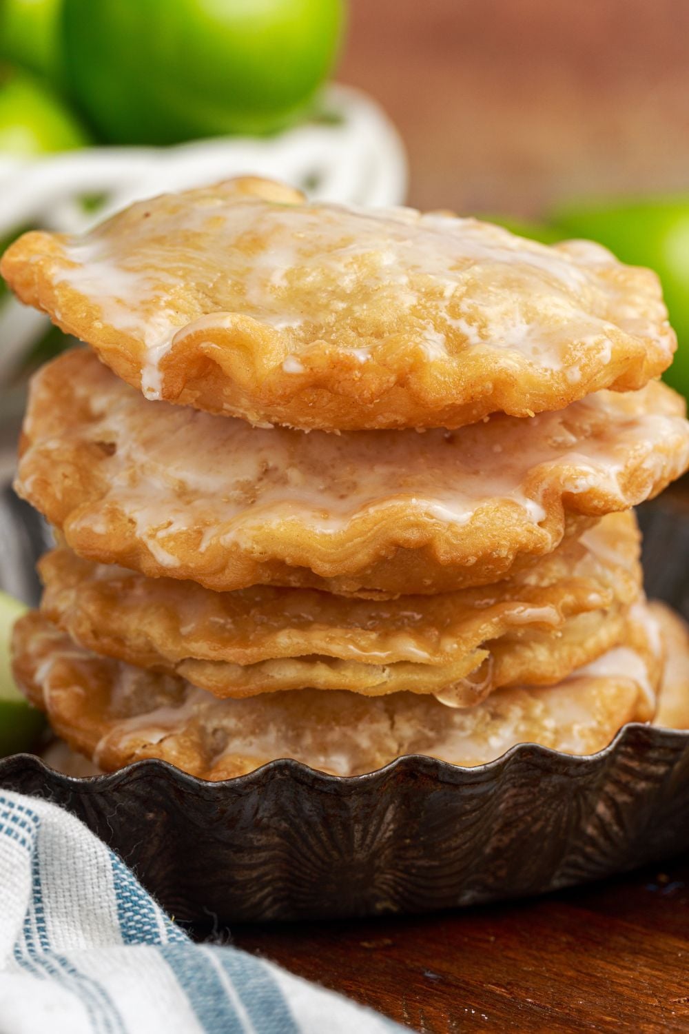 Deep Fried Apple Hand Pies stacked on table with more apples to side and towel in front