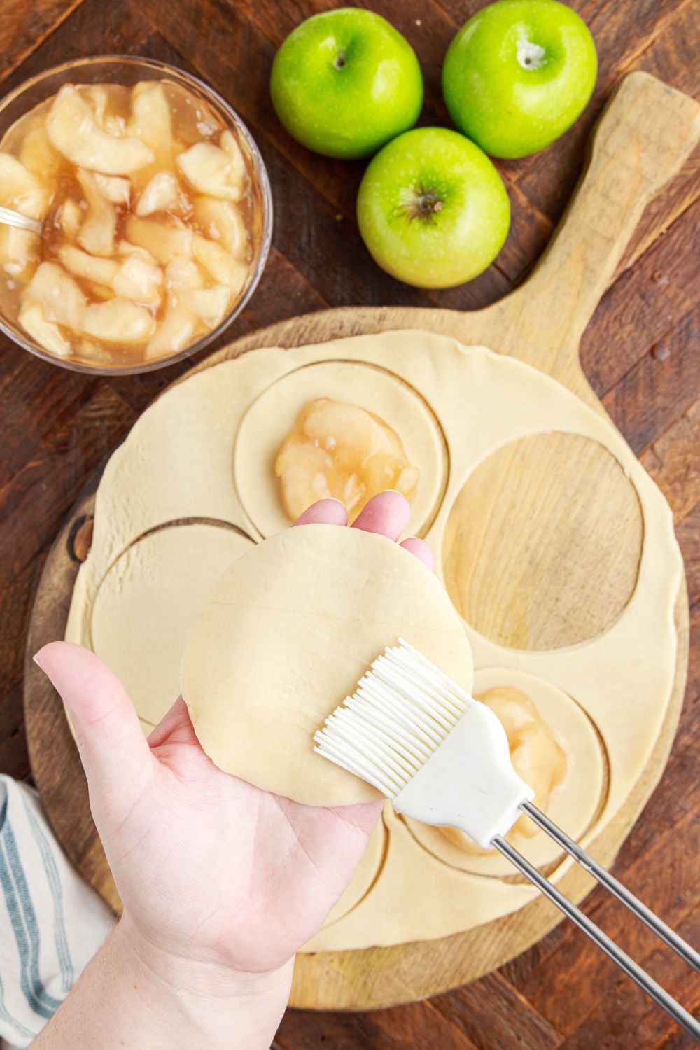 Deep Fried Apple Hand Pies being made on table being brushed and pie filling in circles