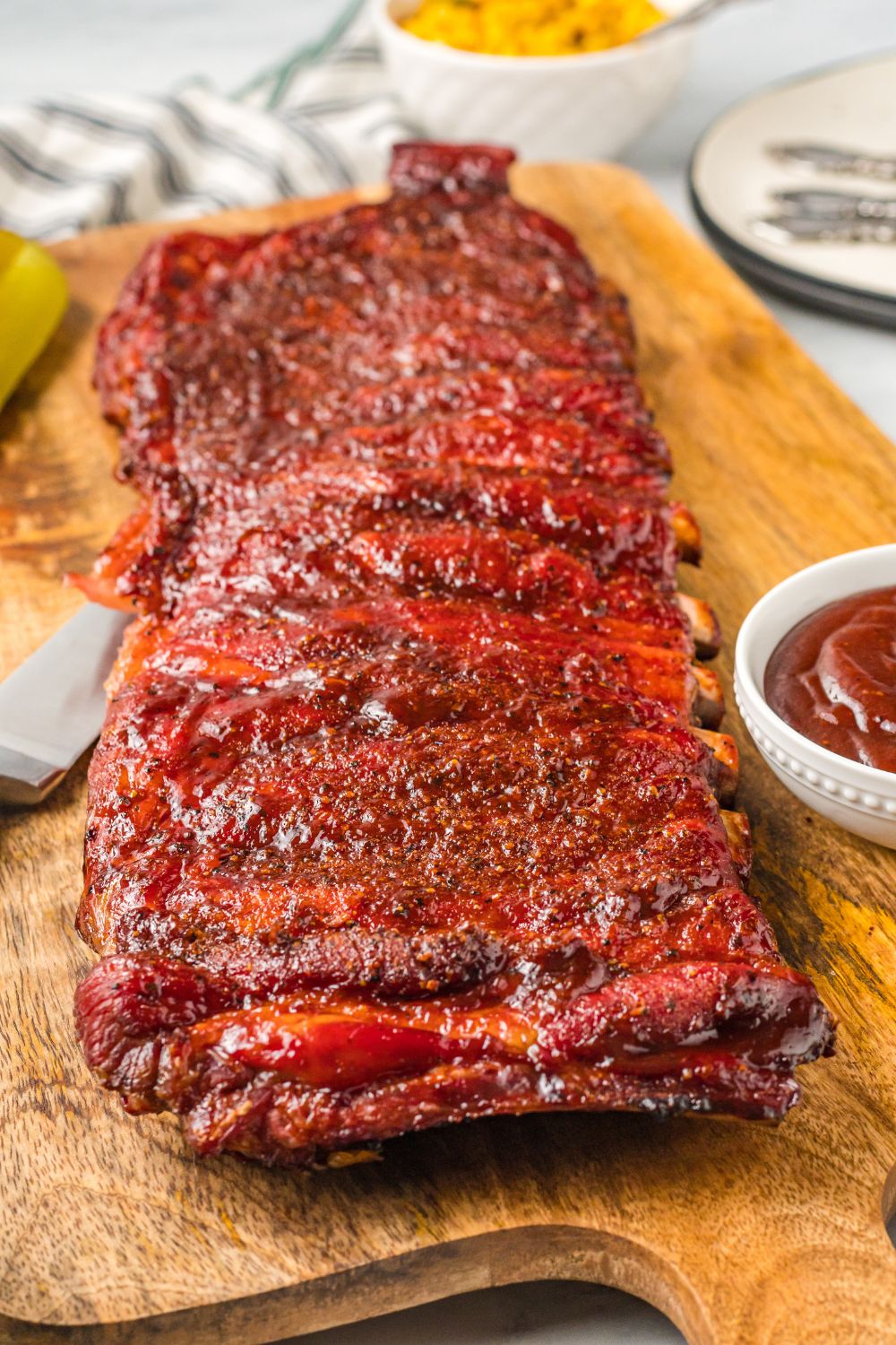 Grilled BBQ Baby Back Ribs on a wooden cutting board with more sauce in a bowl