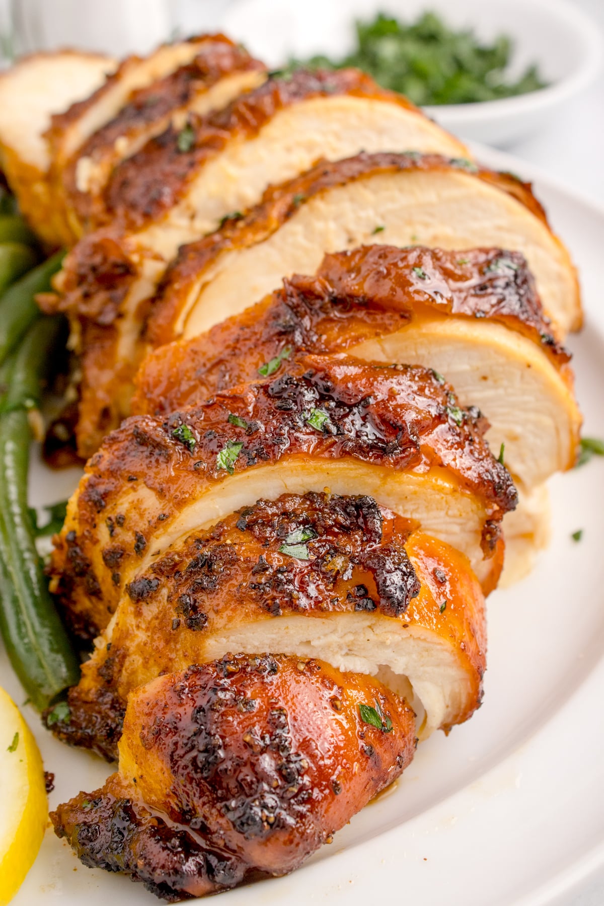Air Fryer Chicken Breast sliced on table with some vegetables to side of the chicken