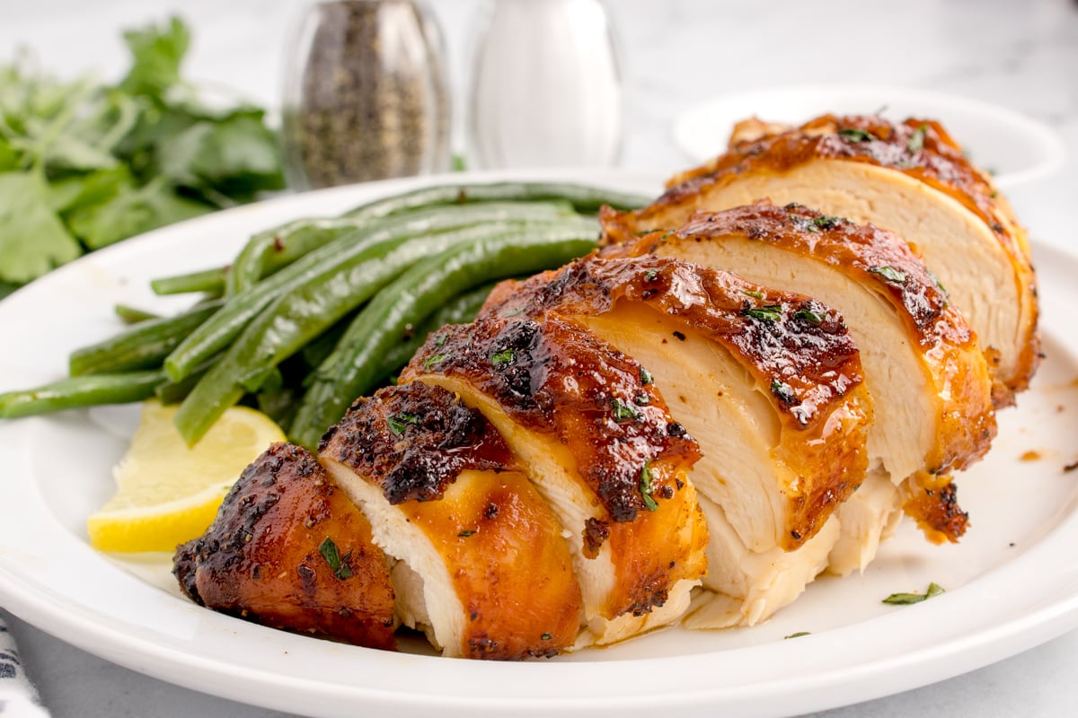 side view of the Air Fryer Chicken Breast sliced on table with some vegetables to side of the chicken
