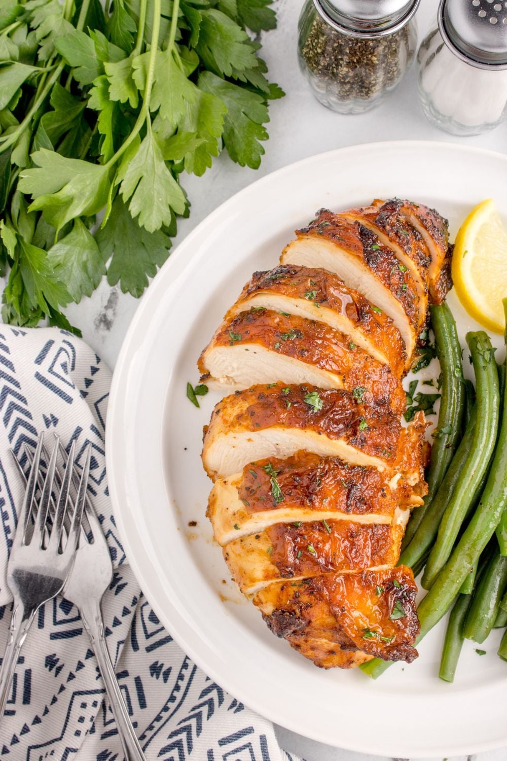 Air Fryer Chicken Breast sliced and placed on plate with lemon wedge and green beans cooked up