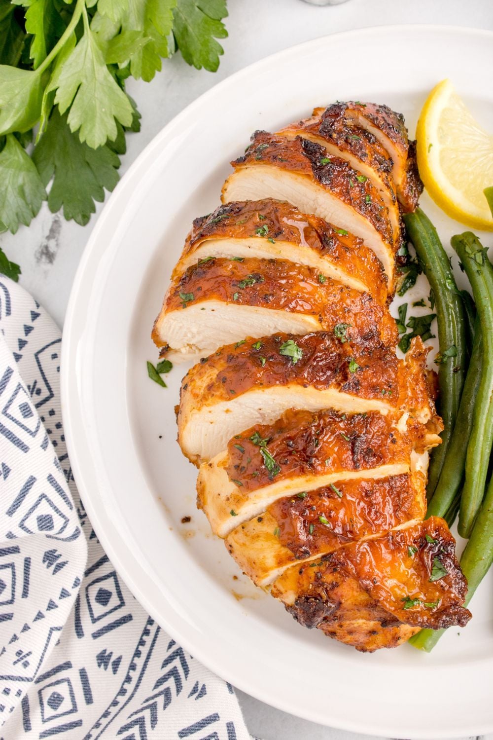 Air Fryer Chicken Breast sliced on plate with some green beans and lemon wedge to side on plate
