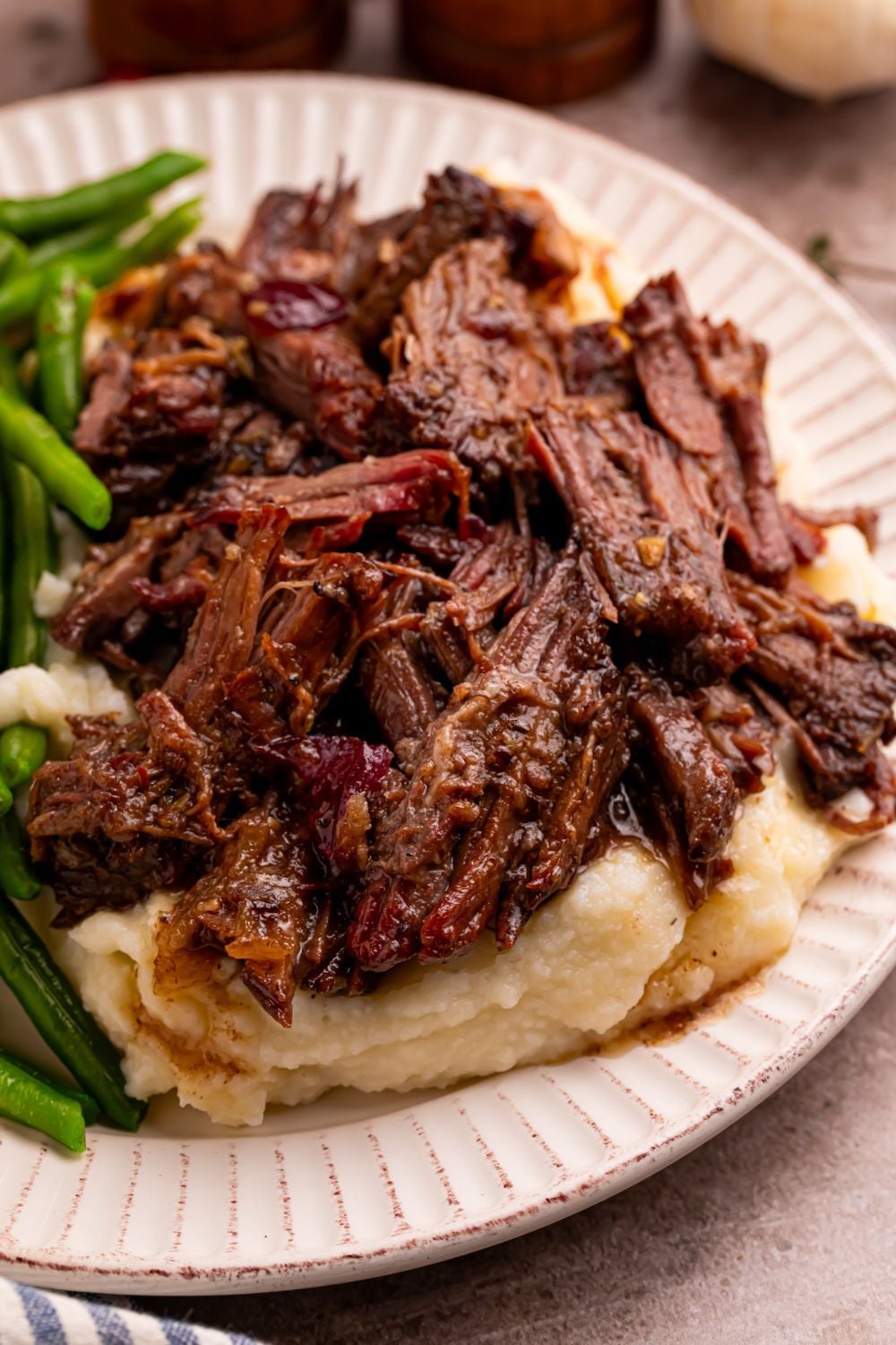 Cranberry Pot Roast shredded on plate with mashed potatoes under and a side of green beans
