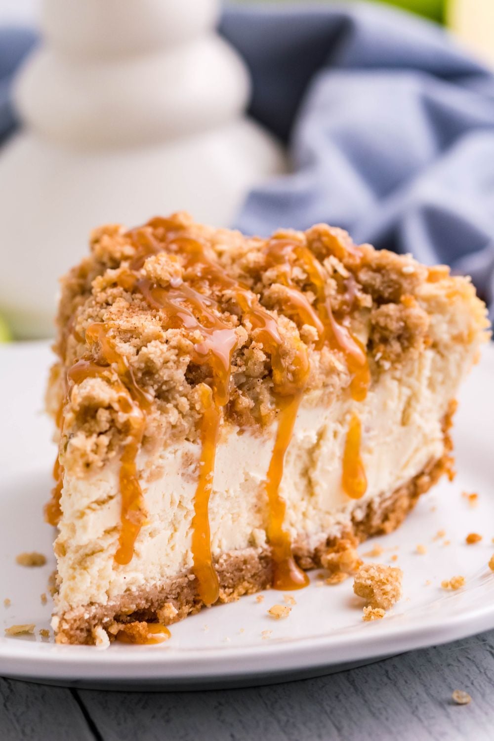 close up of Caramel Apple Crisp Cheesecake slice on plate with a blue towel behind it on table