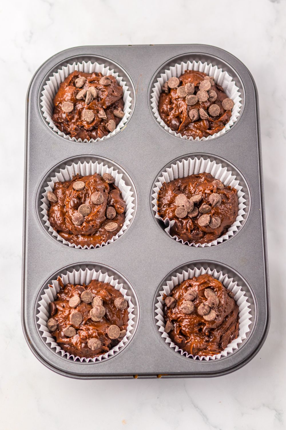 raw Costco Double Chocolate Muffin batter in a muffin pan on table