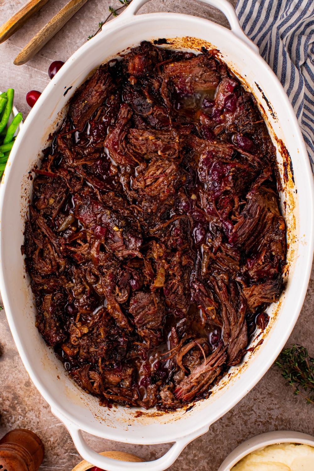 Cranberry Pot Roast shredded and in a pan on table with a towel to side of pan