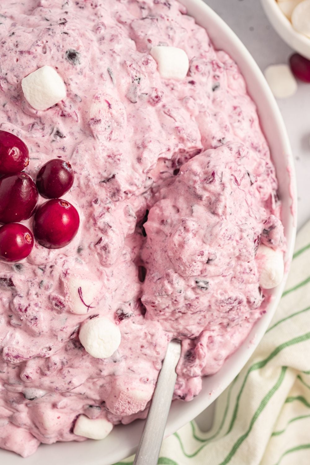 Cranberry Fluff Salad in a white bowl with fresh cranberries in center, and a pin striped towel around side of bowl