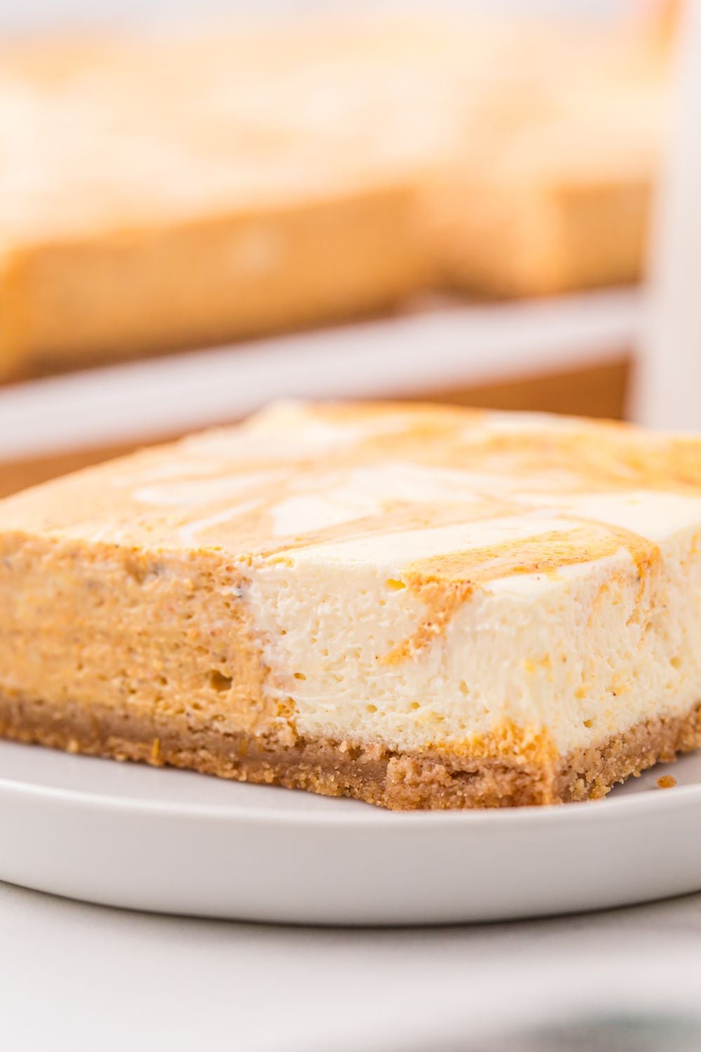 Swirled Pumpkin Cheesecake Bar on a plate with more bars behind it on table