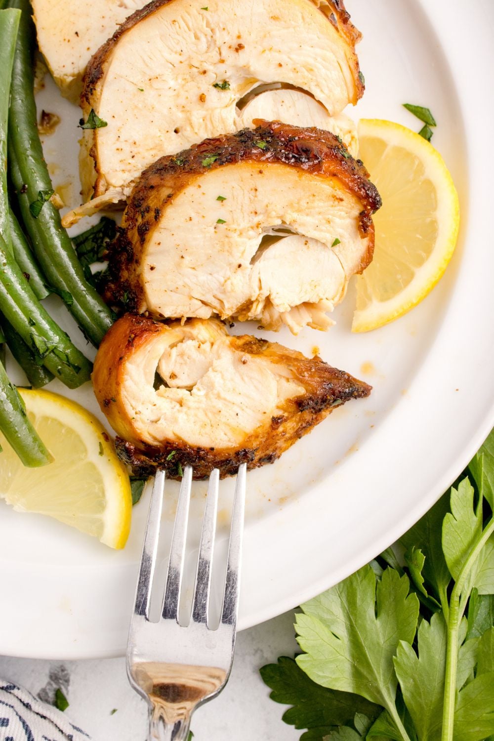 Air Fryer Chicken Breast sliced and placed on plate with lemon and green beans for a meal