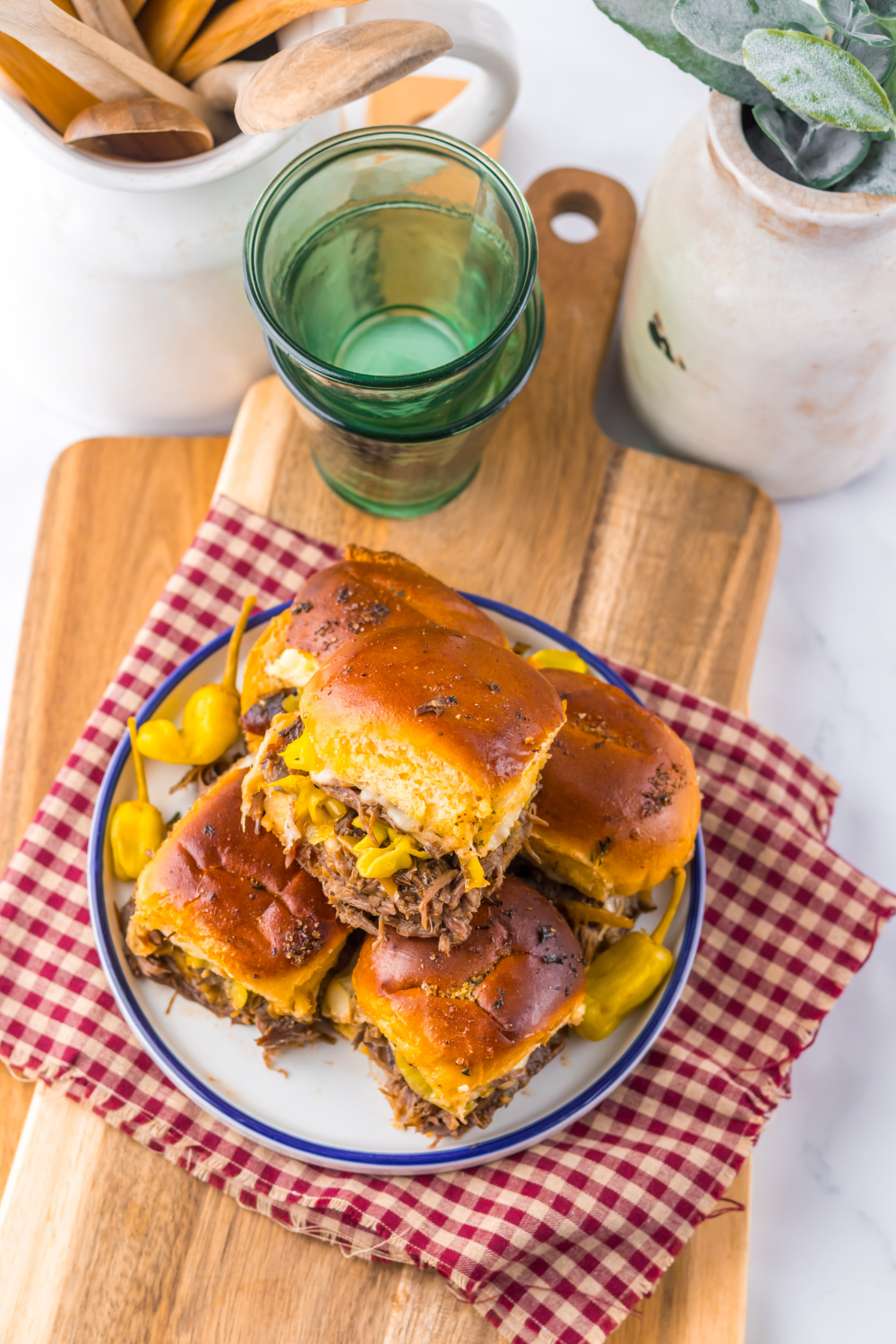 Slow Cooker Mississippi Pot Roast Sliders on a plate with some dishes behind the plate full of burgers 