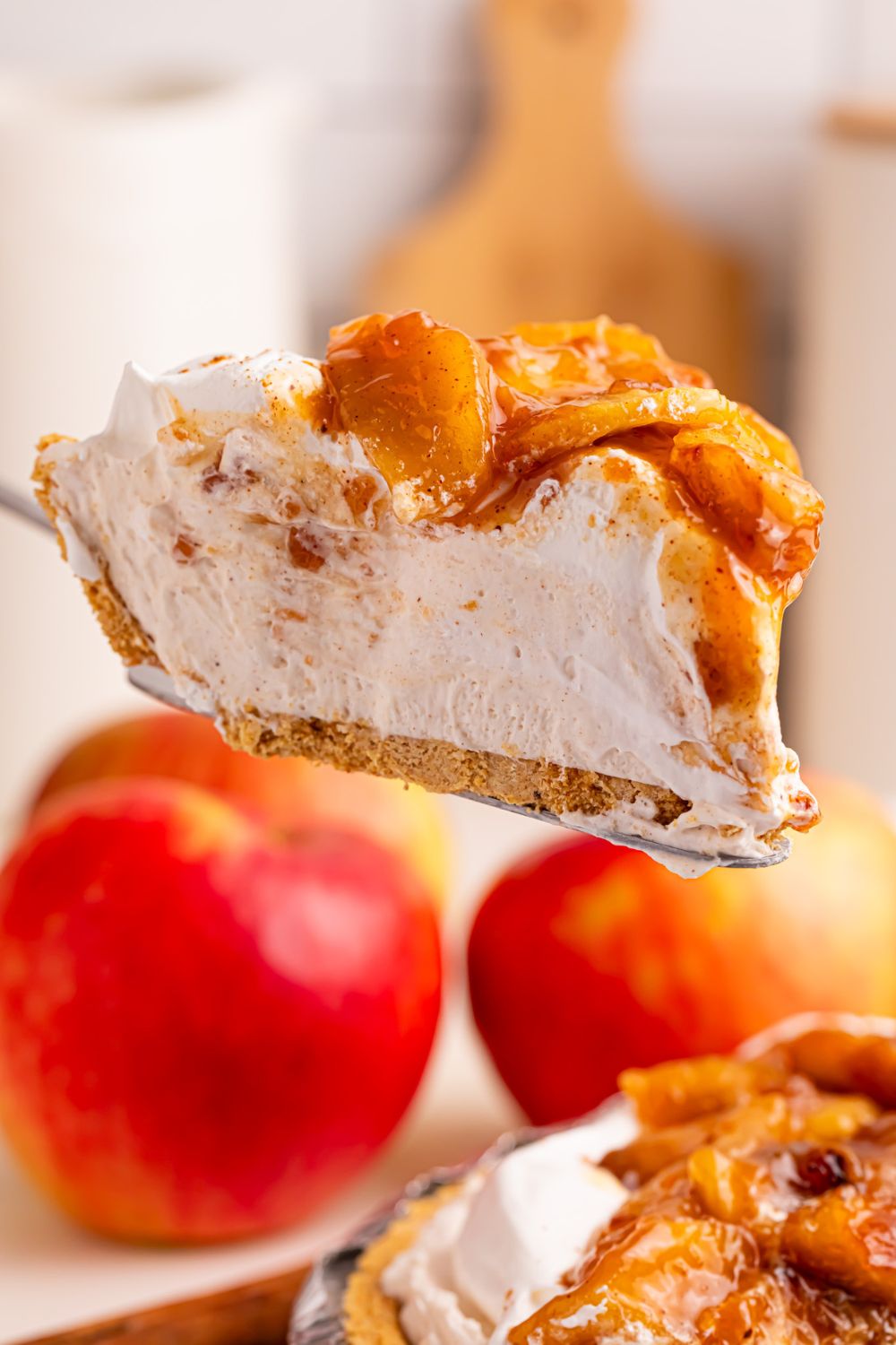 slice of No Bake Apple Cheesecake pie on spatula with red apples