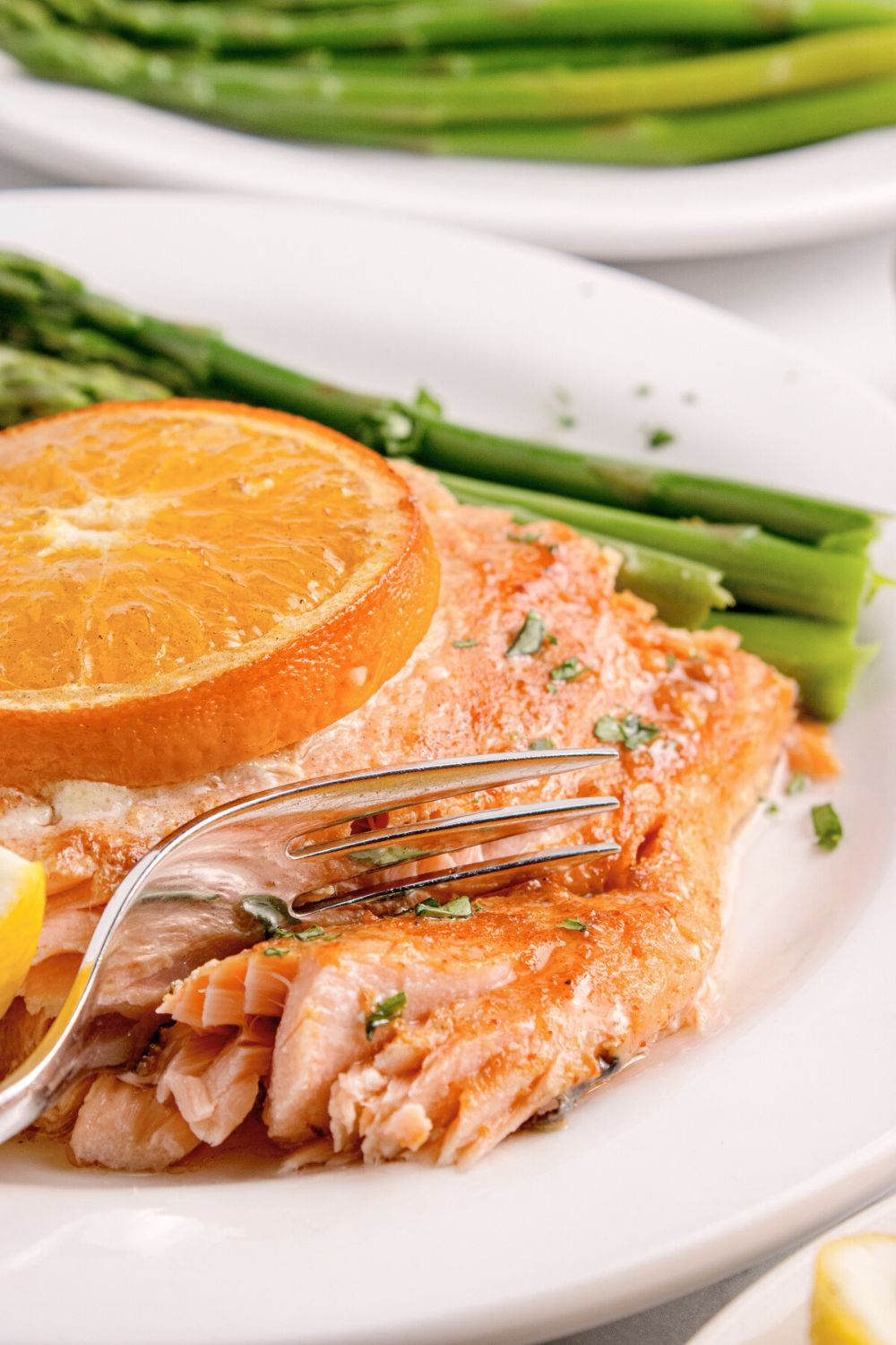 Grilled Honey Mustard Salmon on plate with a fork cutting into salmon with asparagus tose side and on a second plate