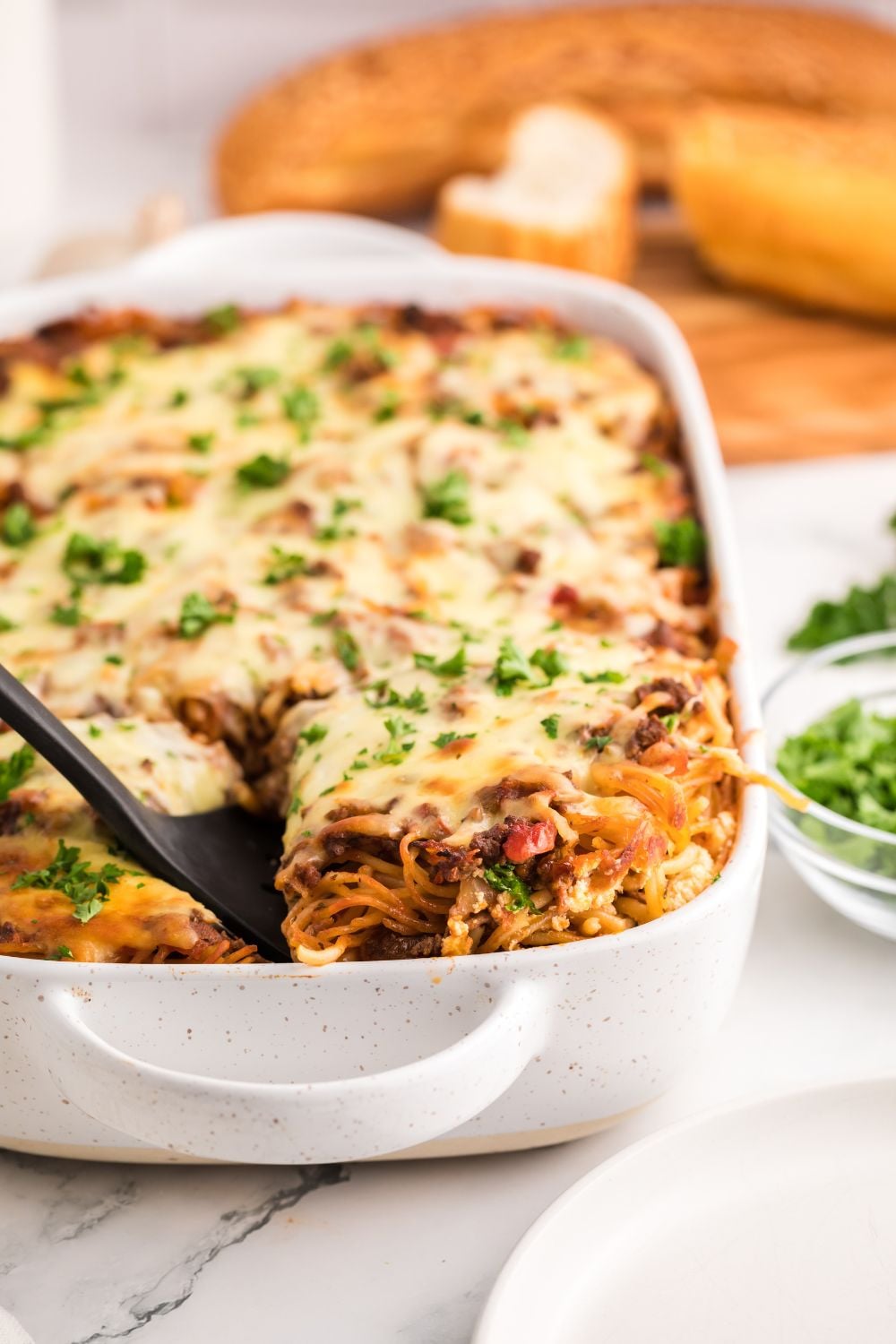 Million Dollar Spaghetti Casserole in a pan with bread behind on a cutting board