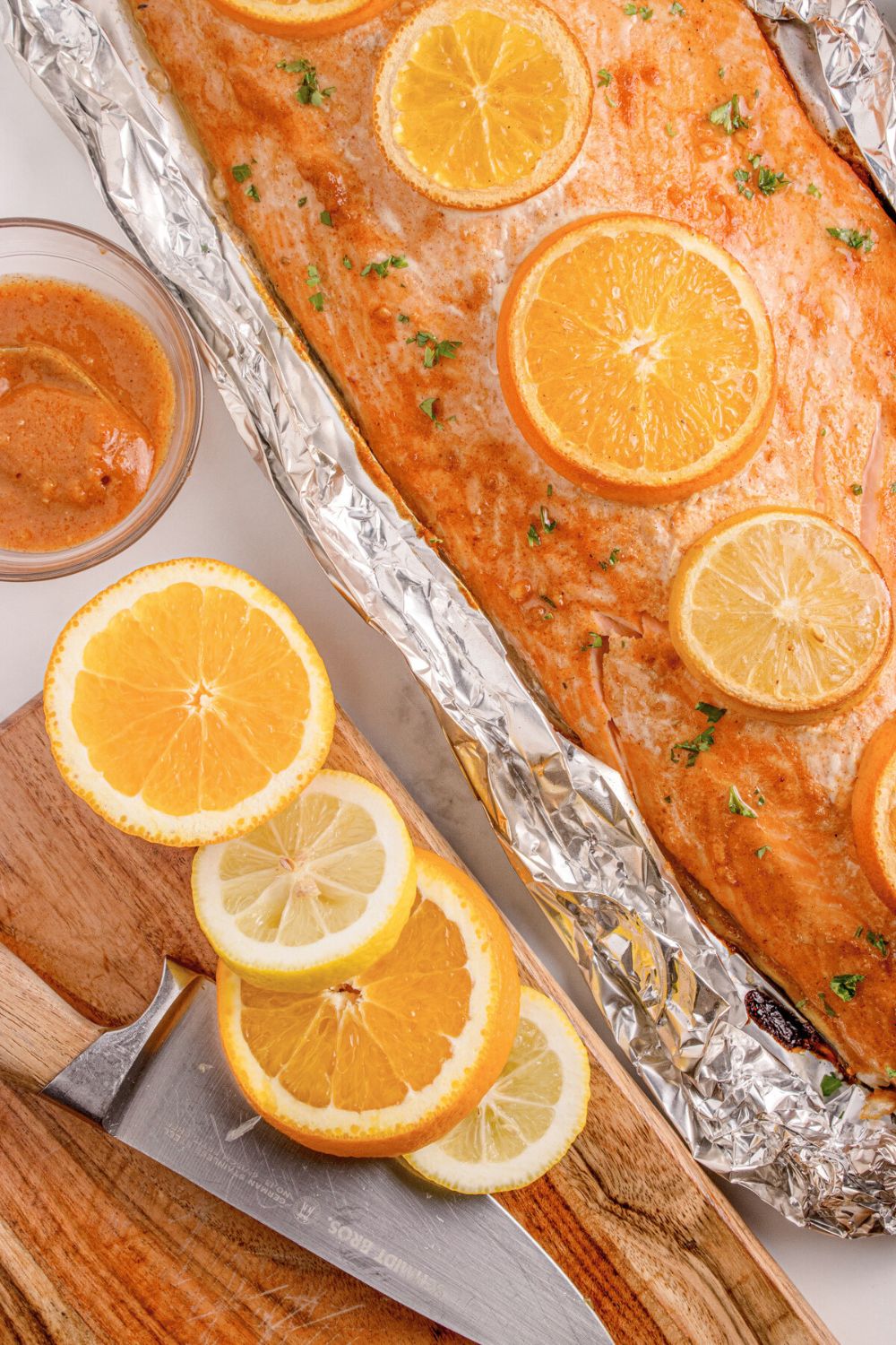 Grilled Honey Mustard Salmon in Foil sitting on table, with more oranges sliced and placed on cutting board to side