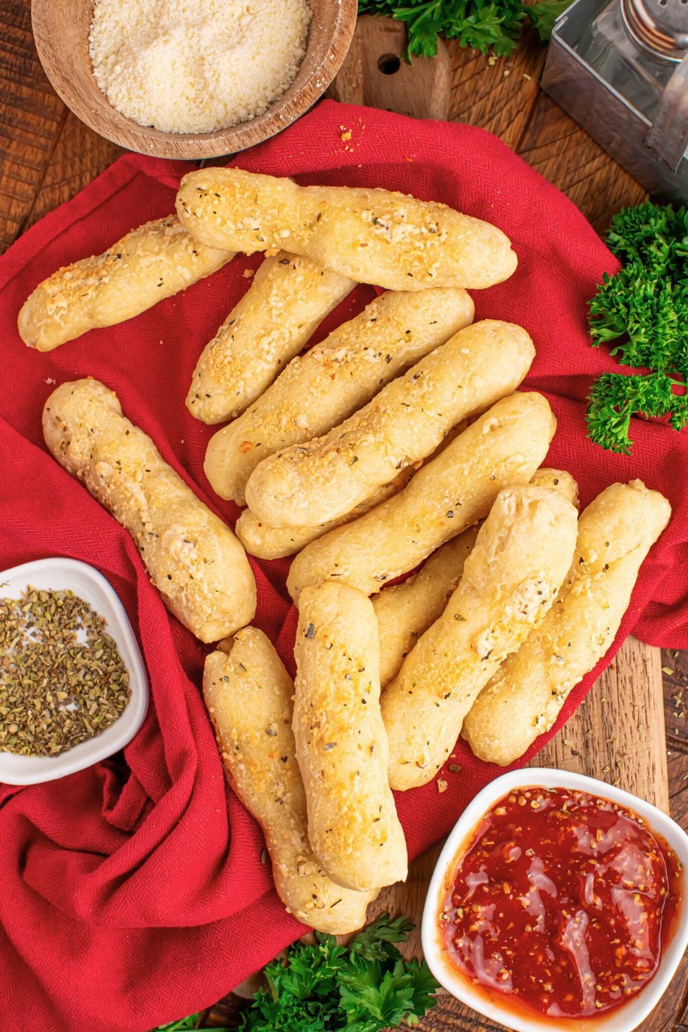 2 ingredient breadsticks scattered on table with sauce in bowl and seasoning in another bowl