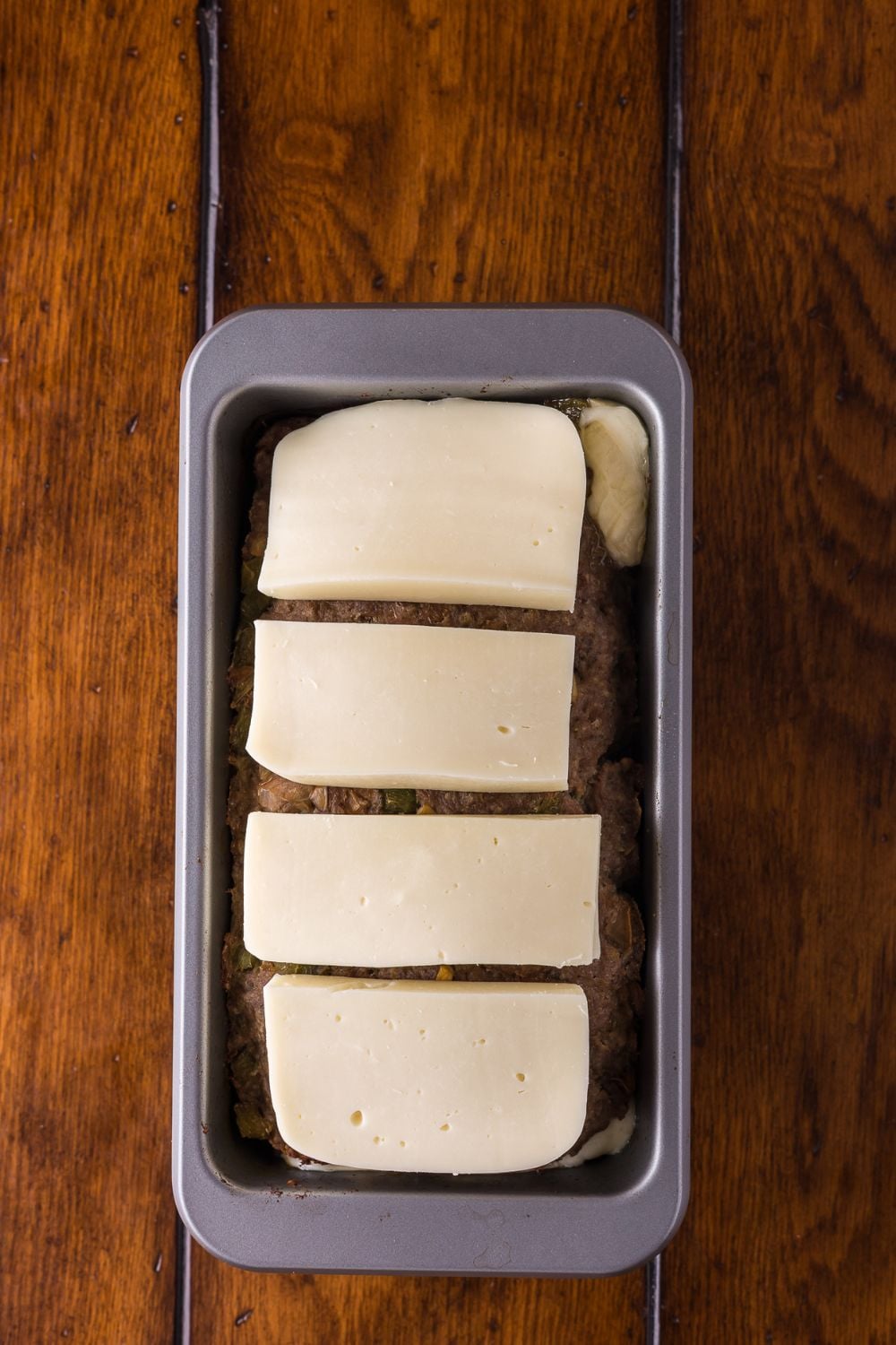slices of provolone sitting on top of a raw Stuffed Philly Cheesesteak Meatloaf in loaf pan
