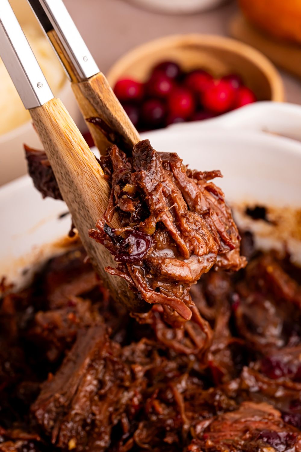 Cranberry Pot Roast in a pan and tongs lifting up some of the meat