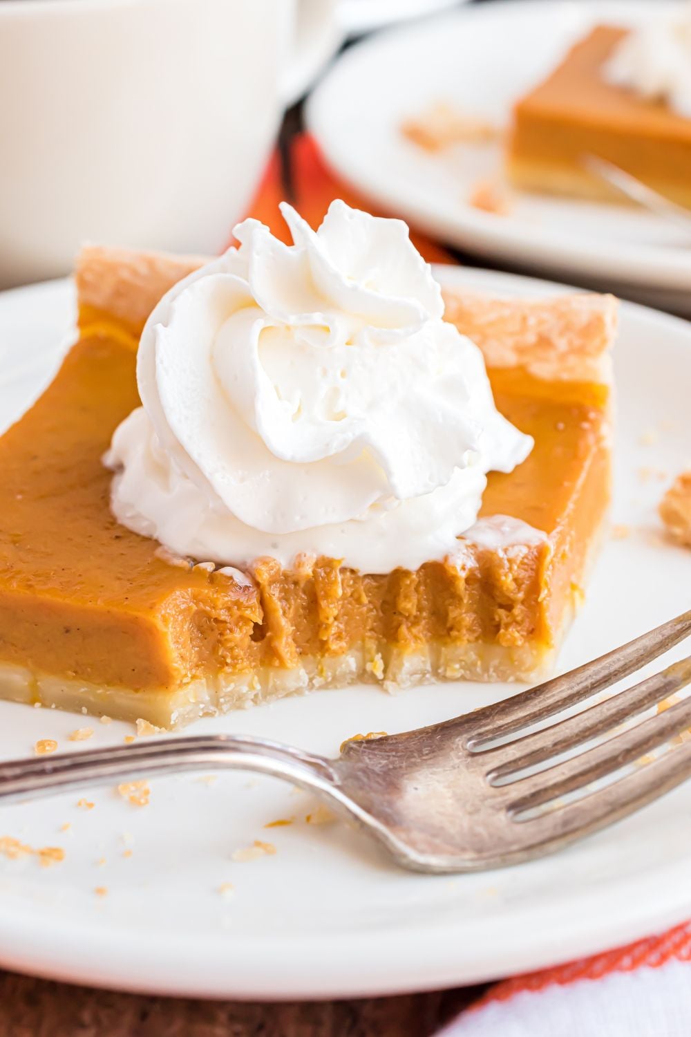 Homemade pumpkin pie squares sitting on white plates with one with a bite taken out with fork marks in the pie with a fork sitting in front of slice of pie on wood table
