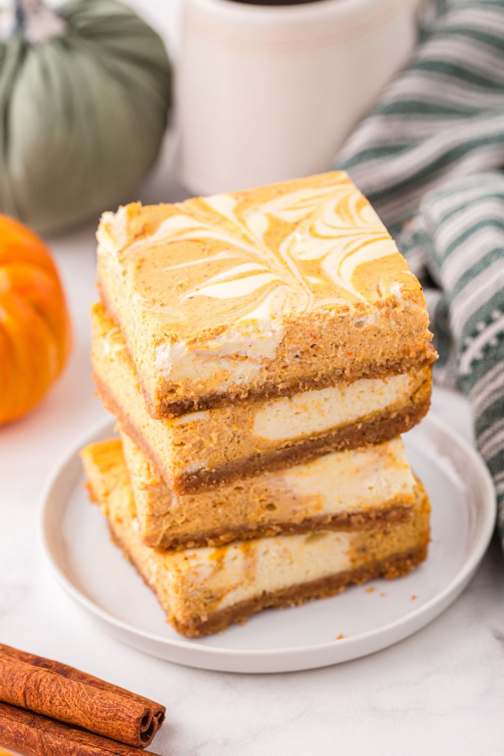 plate with a stack of Swirled Pumpkin Cheesecake Bars on it and coffee in a cup behind it
