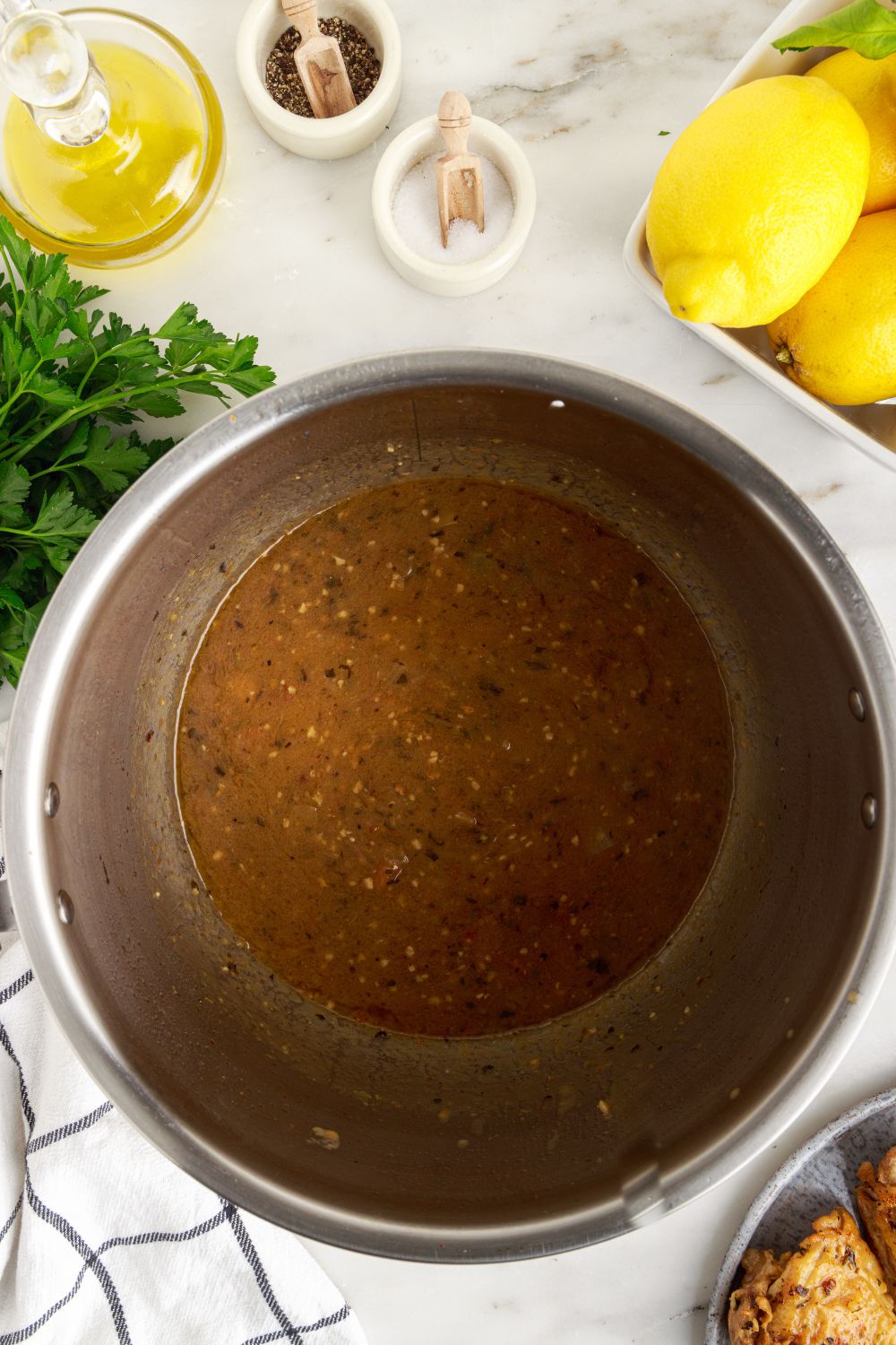 overhead look of instant pot with butter sauce inside and fresh herbs and lemons on table behind it