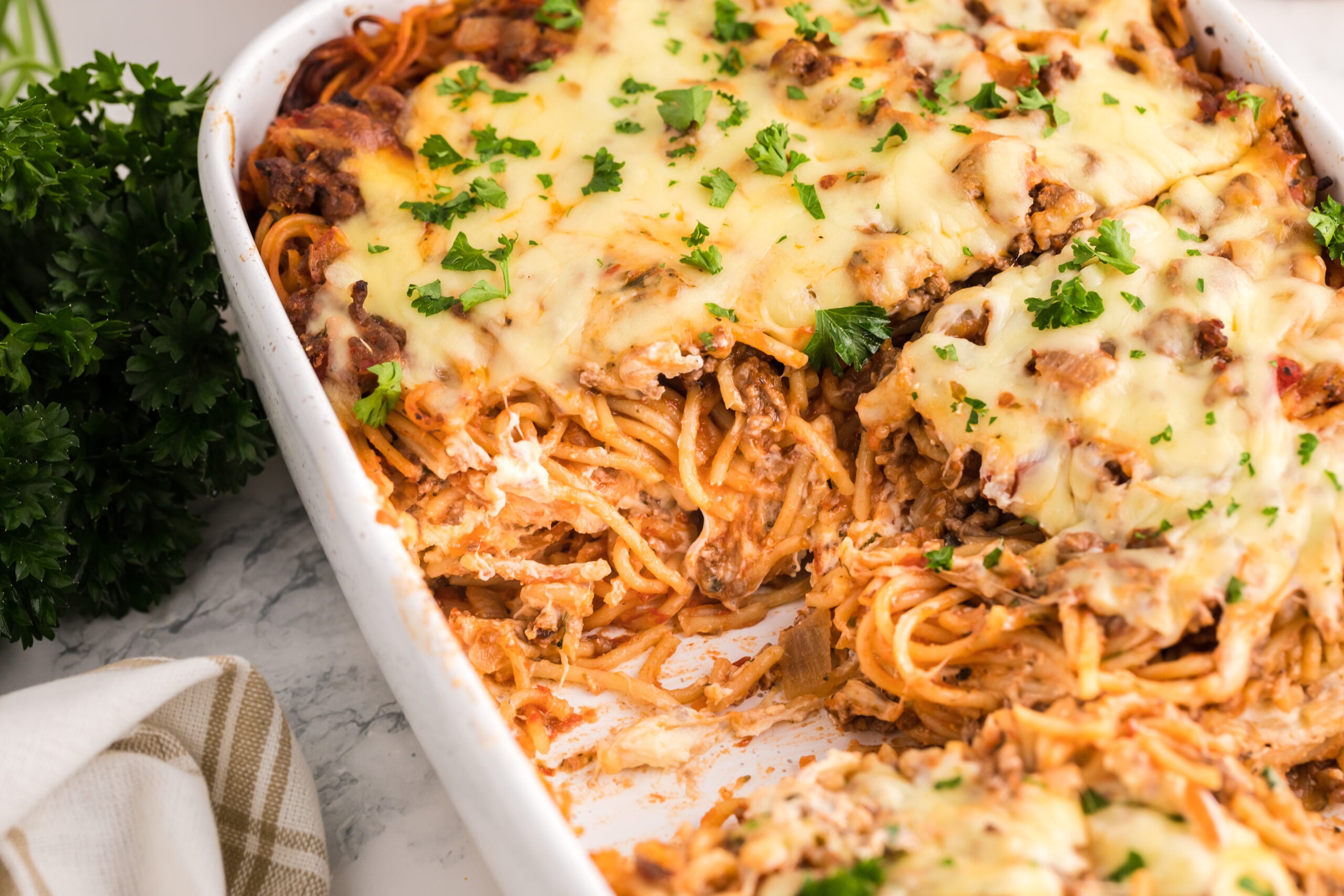 Million Dollar Spaghetti Casserole in a white baking dish with a couple slices removed