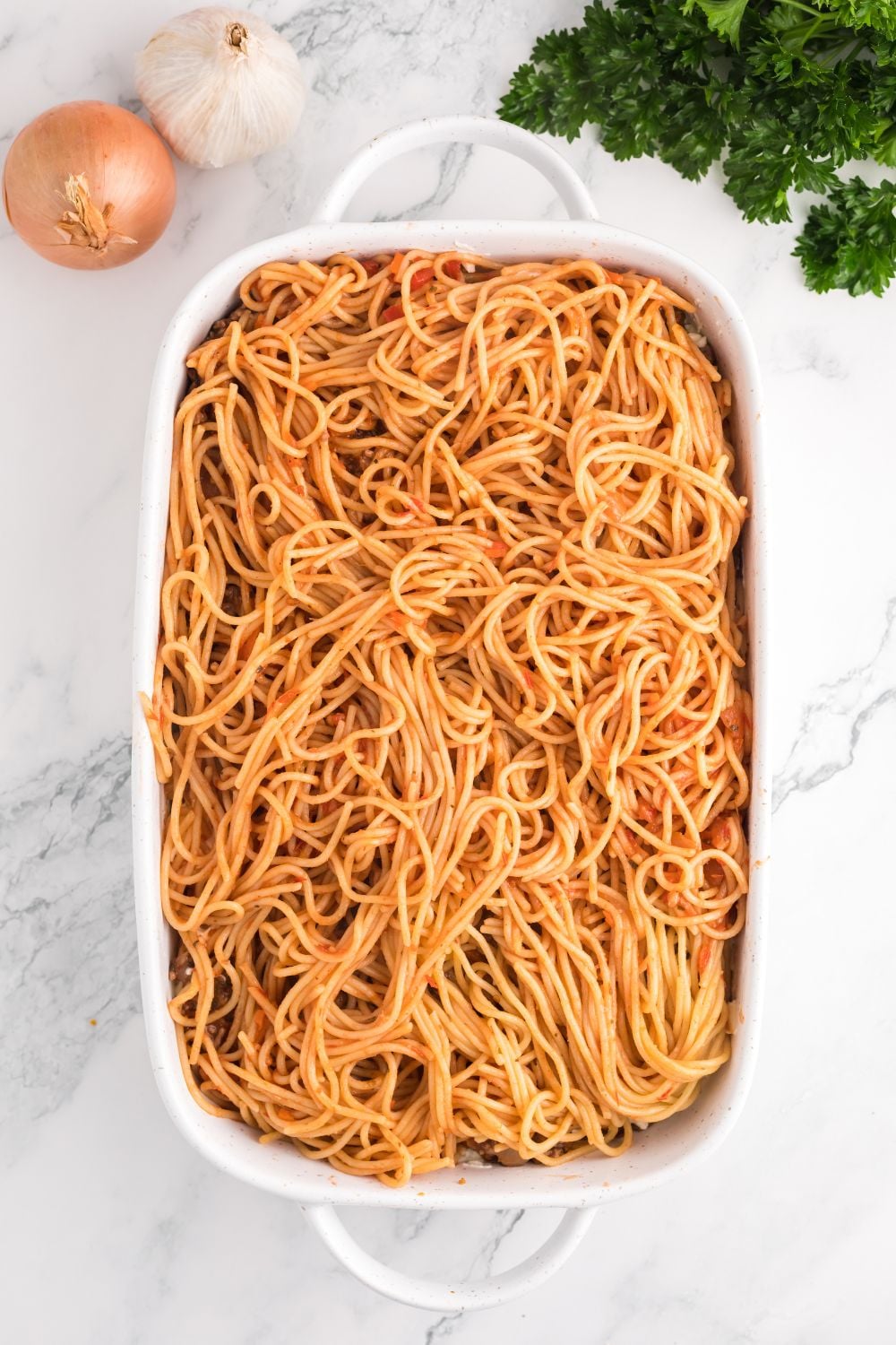 Million Dollar Spaghetti Casserole being assembled in a pan on table