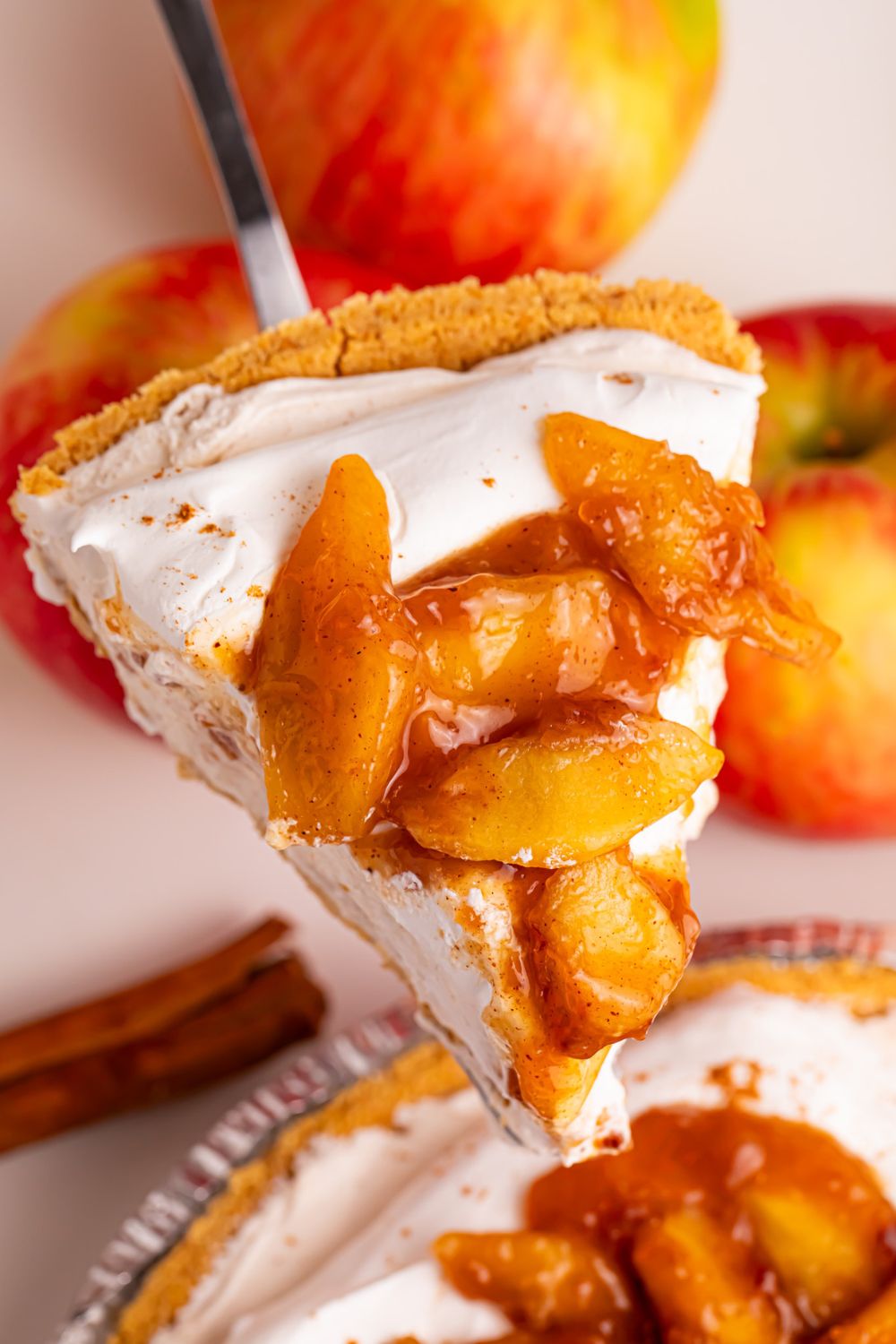 slice of No Bake Apple Cheesecake pie slice being lifted above pie dish on a table