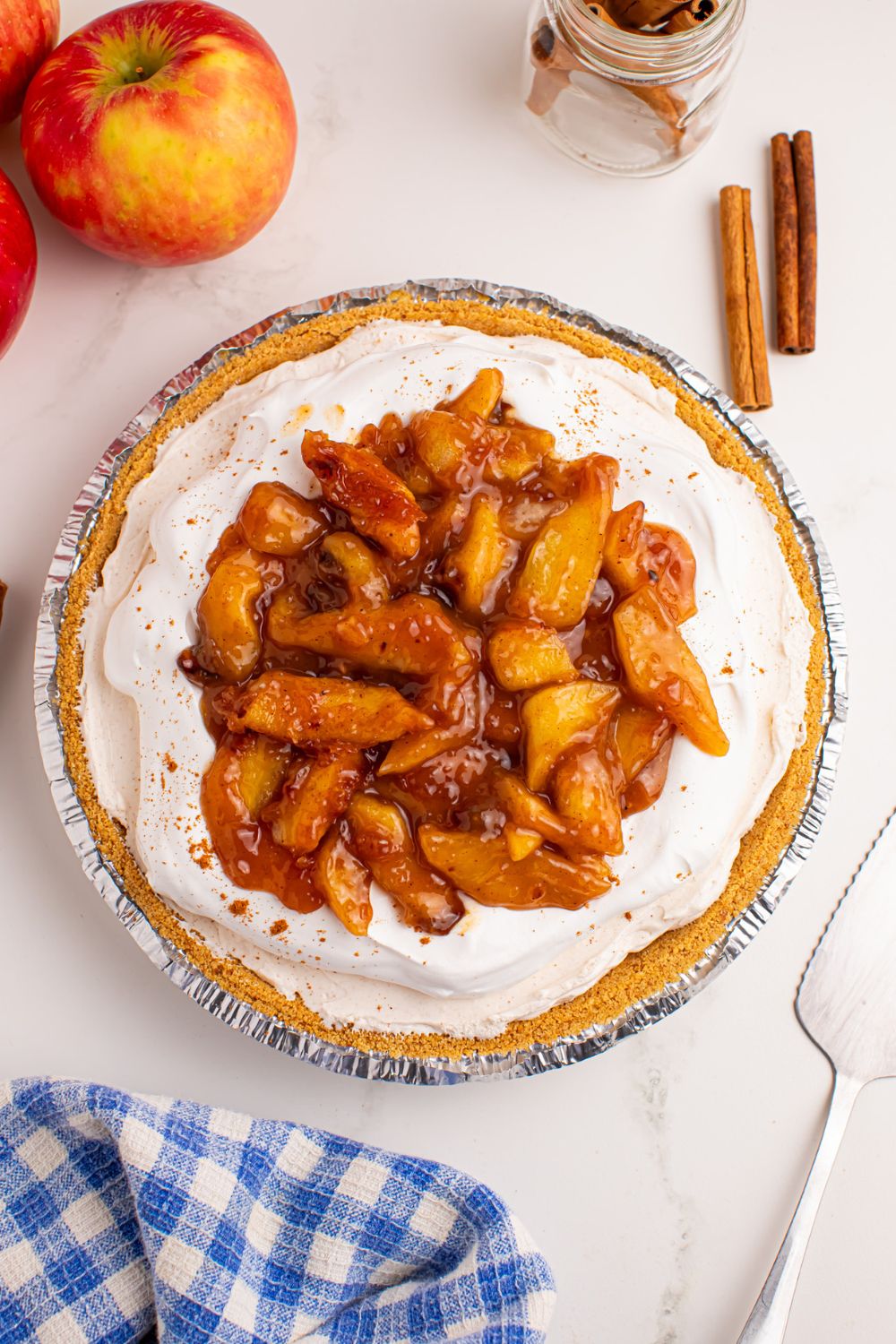 overhead look of table with No Bake Apple Cheesecake pie and apples and cinnamon sticks to side