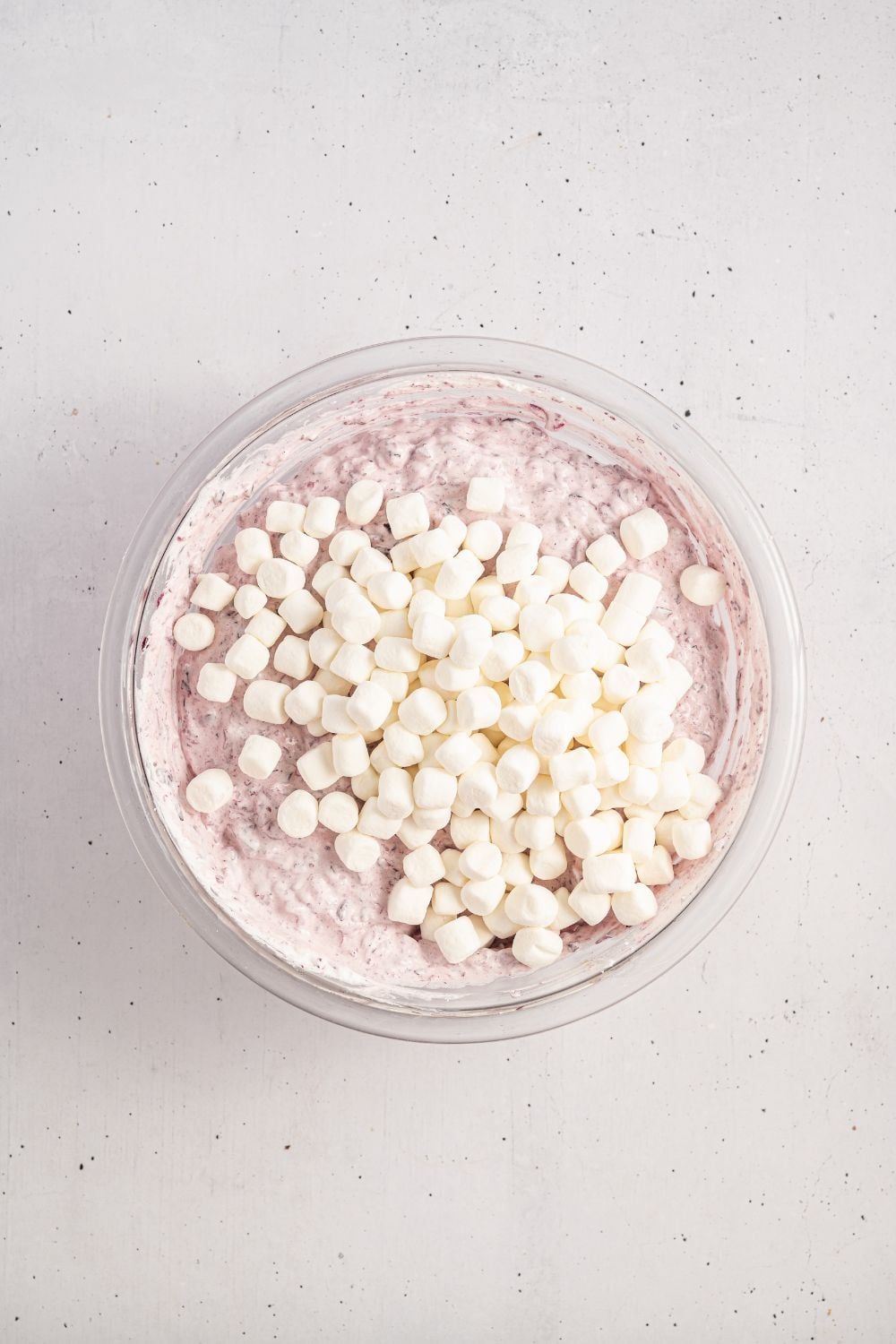 marshmallows on top of cranberry salad being assembled in the glass bowl