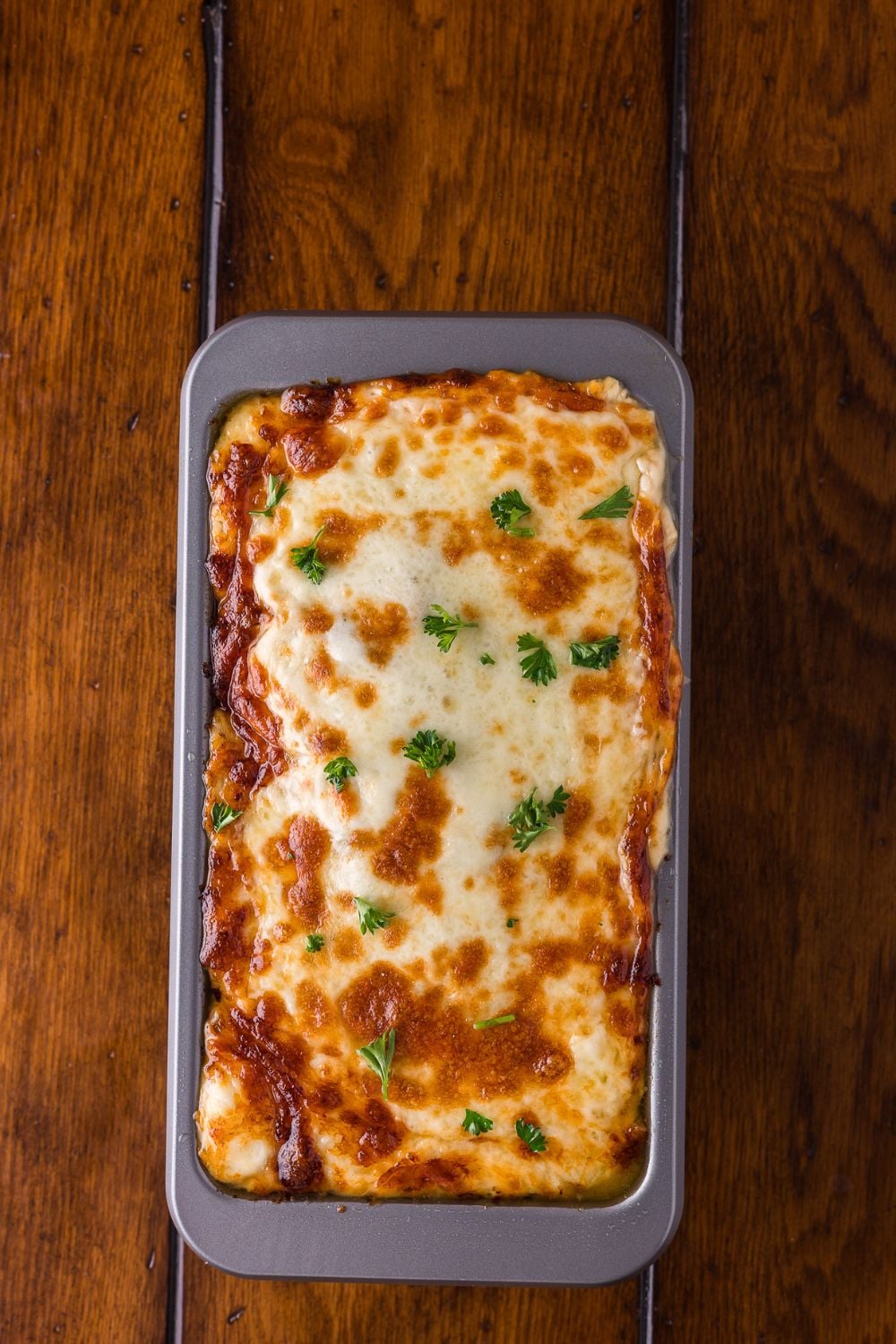 Stuffed Philly Cheesesteak Meatloaf baked and sitting in a loaf pan on wooden table
