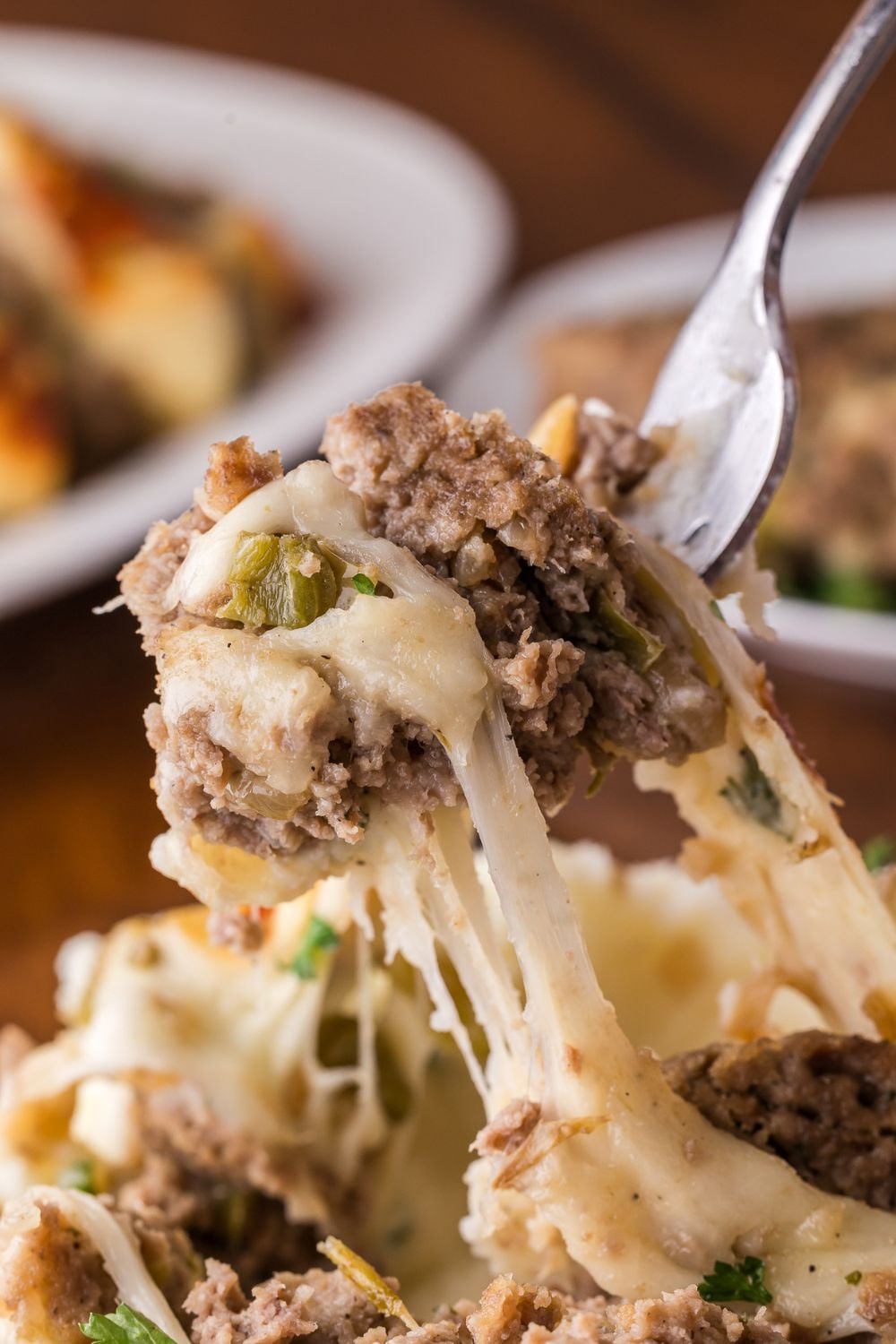 fork with a bunch of cheesy Stuffed Philly Cheesesteak Meatloaf being lifted up off a plate full of more meatloaf sitting on wooden table