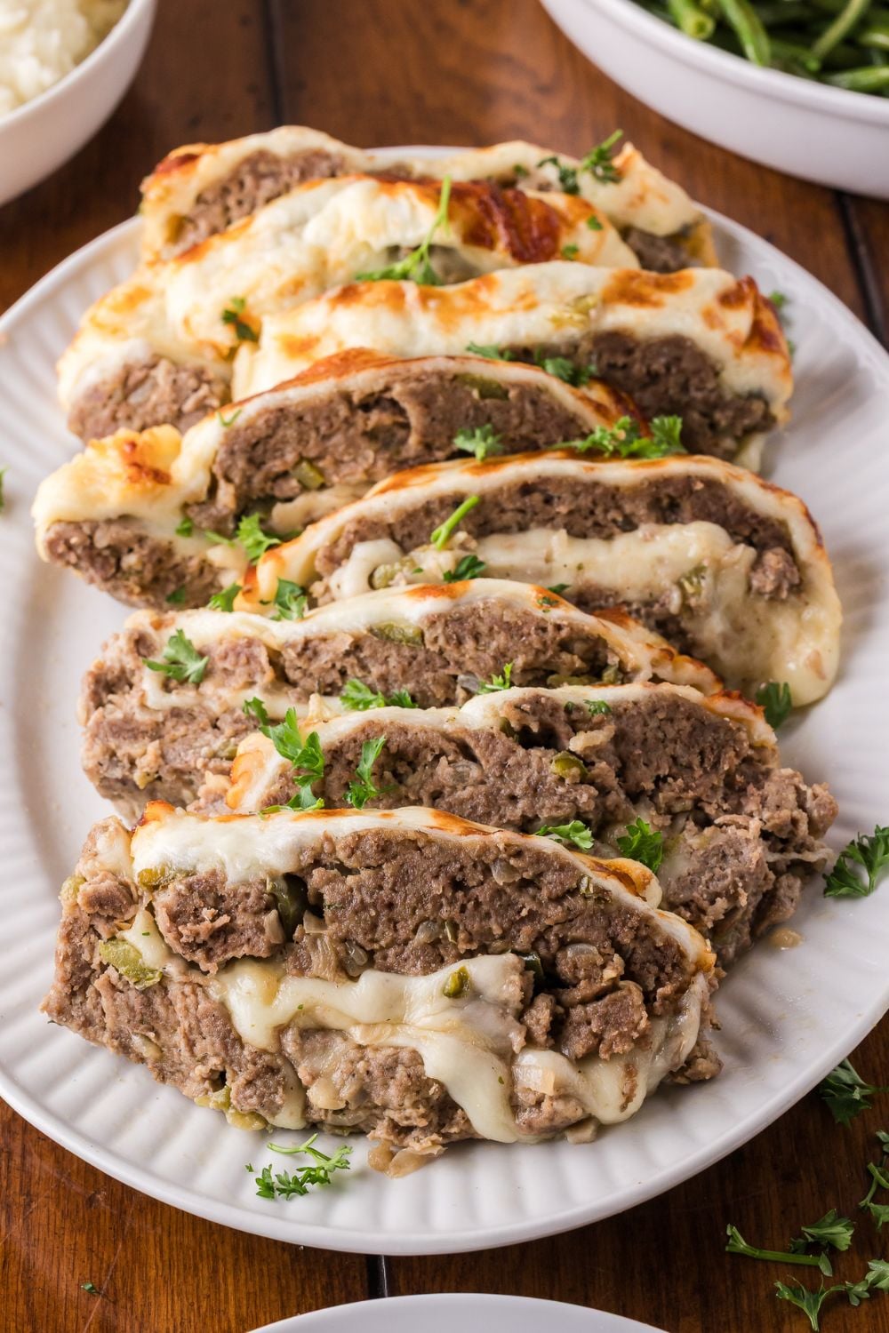 large platter sitting on table that has sliced Stuffed Philly Cheesesteak Meatloaf on it, and other platters with food for serving up a meal for a family on wooden table