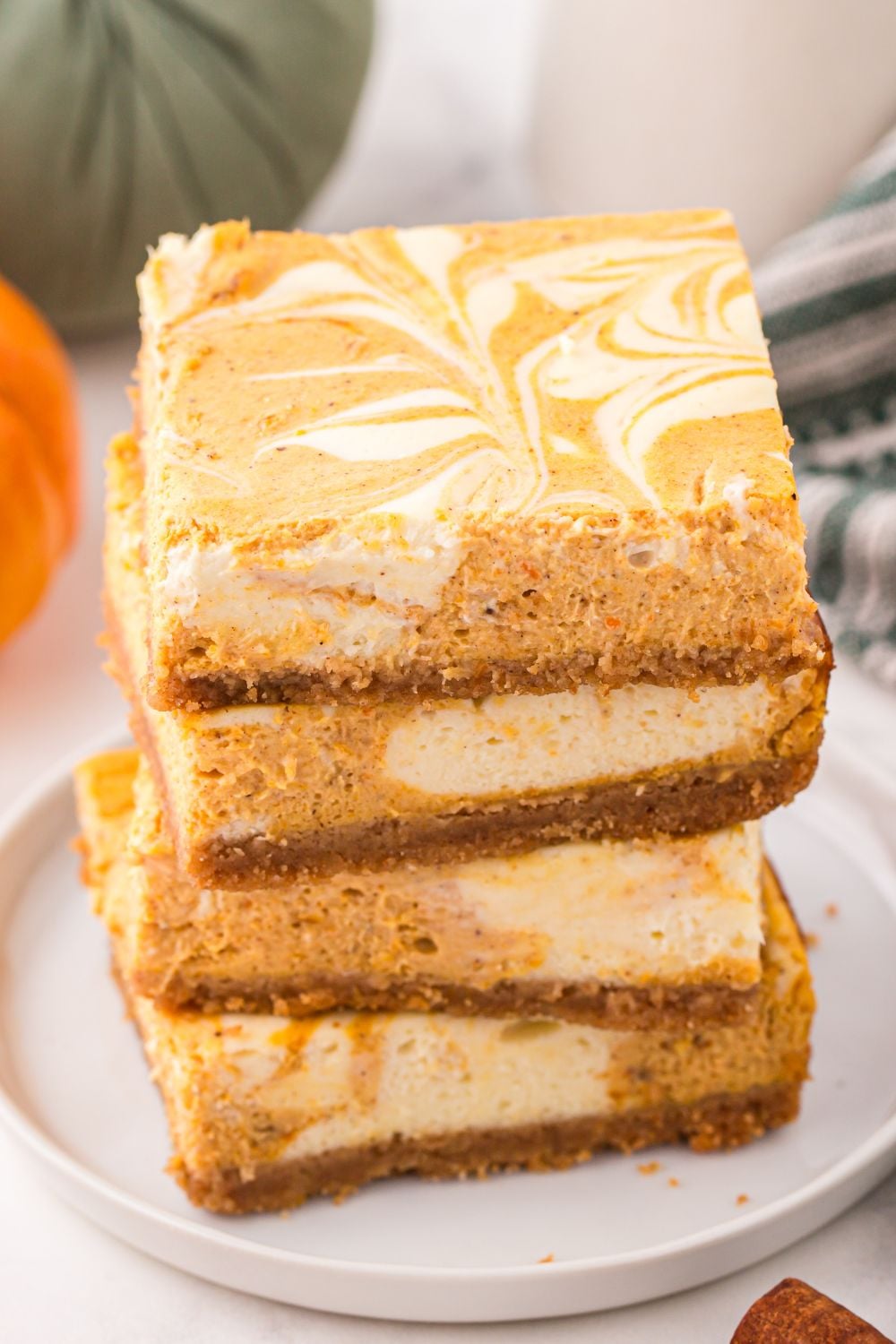 Swirled Pumpkin Cheesecake Bars stacked on a white plate sitting on a table decorated like fall