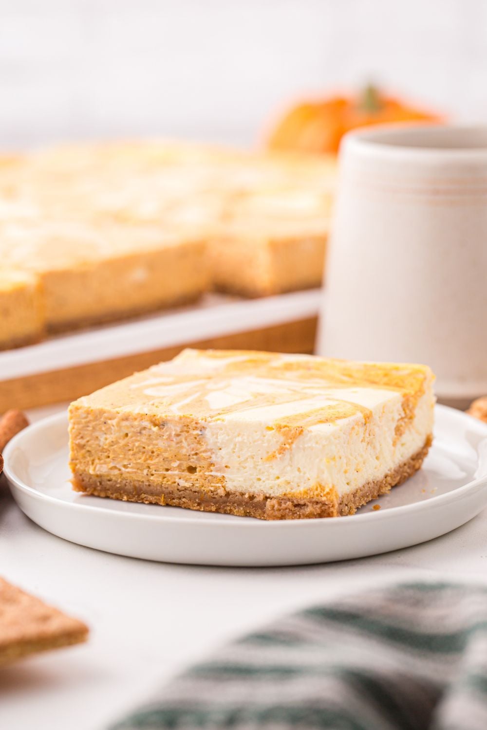 Swirled Pumpkin Cheesecake Bar on plate with the rest of bars behind it on table and a cup of coffee