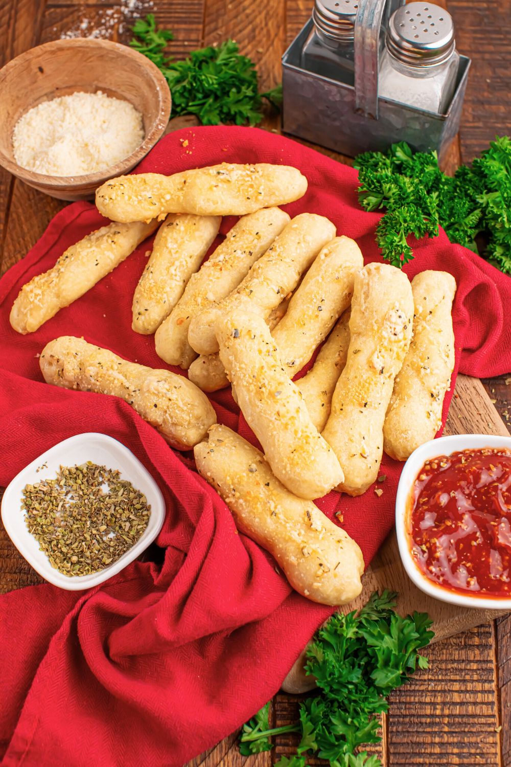 table with 2 Ingredient Garlic Parmesan Breadsticks with sauce, speasoning, and parmesan cheese in a bowl