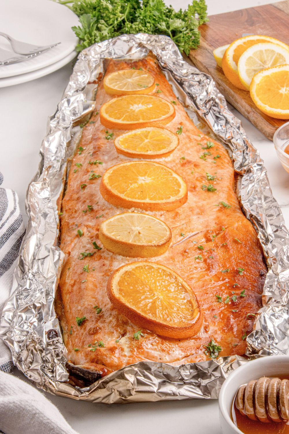 Grilled Honey Mustard Salmon in Foil on table with a bowl of honey to side, sliced oranges, and more around table
