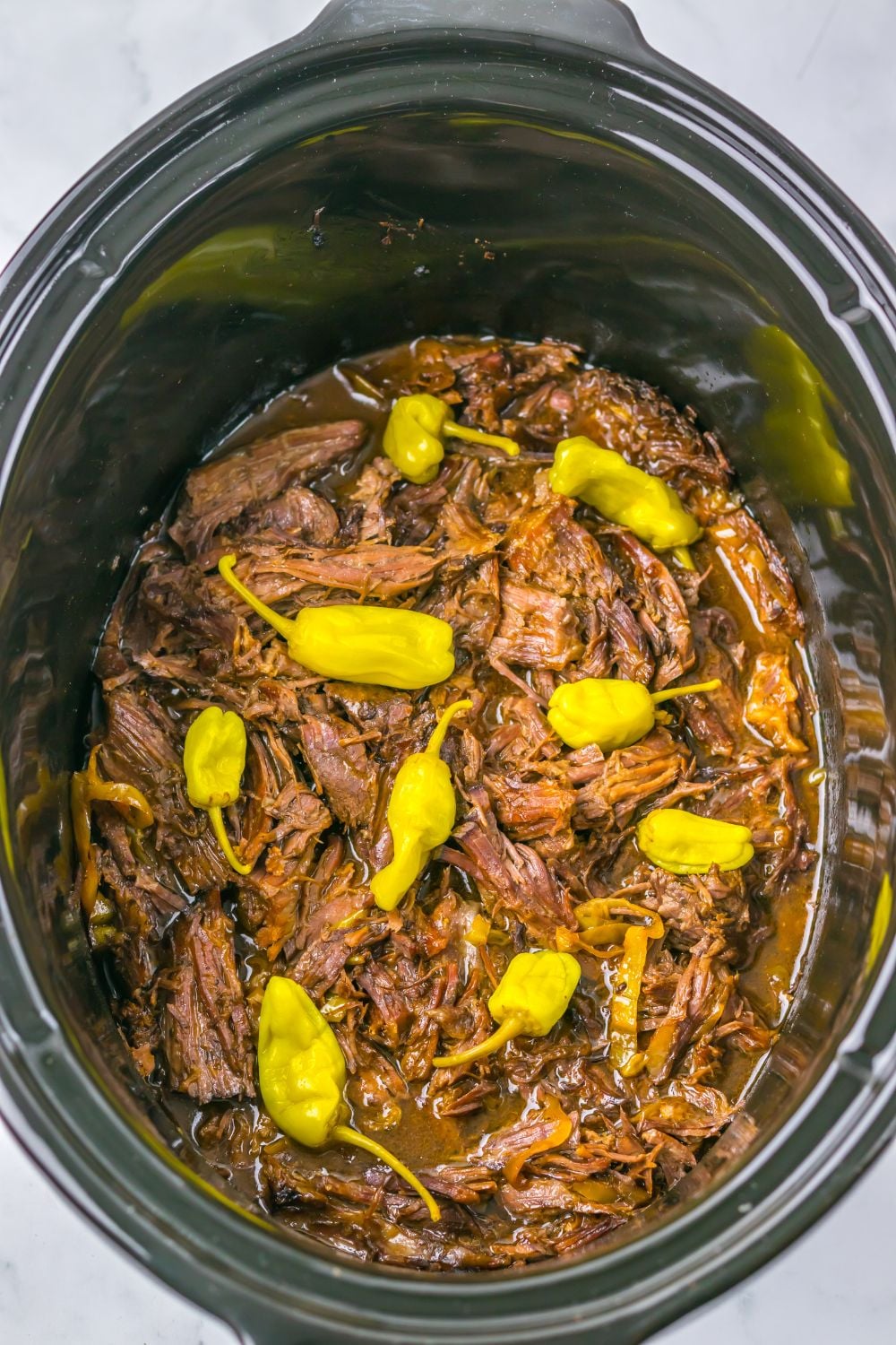 Slow Cooker Mississippi Pot Roast in a slow cooker with more peppers on top 