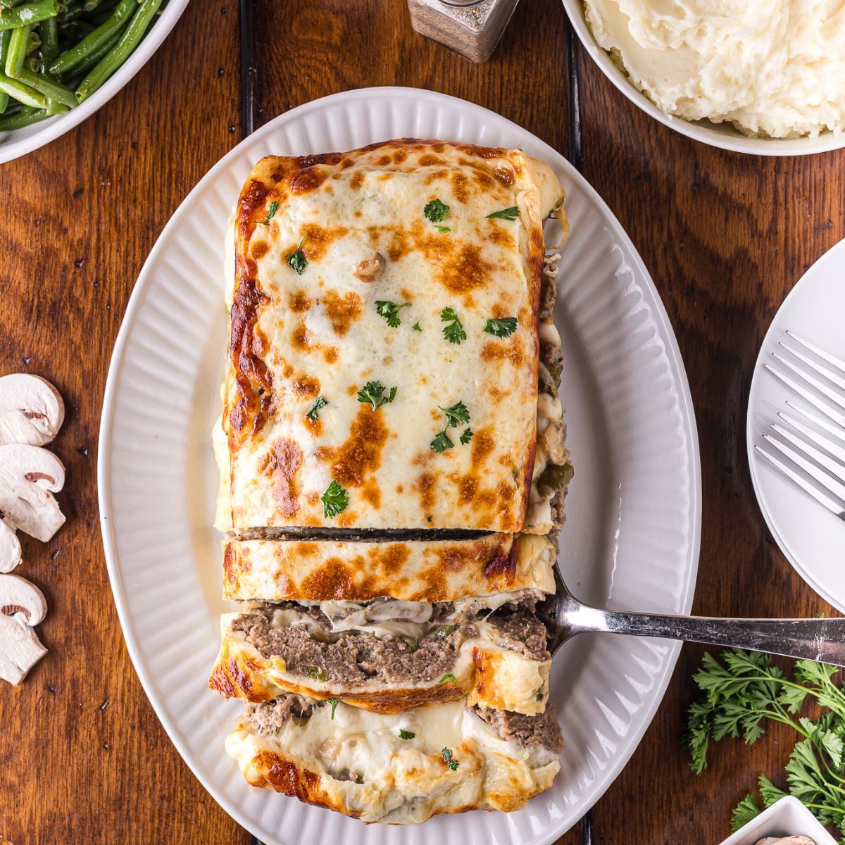 Stuffed Philly Cheesesteak Meatloaf on a white platter on wooden table that is partly sliced and ready to serve