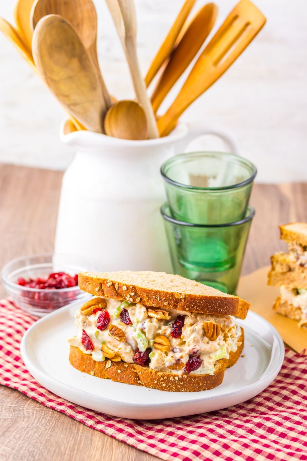 Thanksgiving Turkey Salad on plate with bread, and glasses stacked behind plate with another sandwich to the side 
