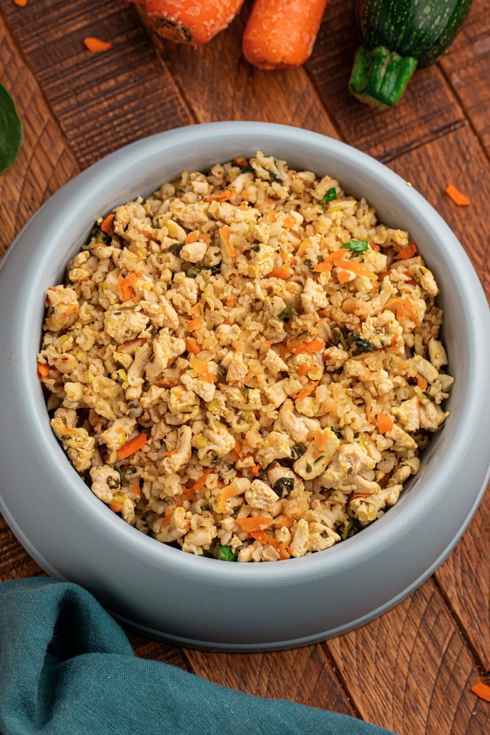 Homemade Turkey and Rice Dog Food with Veggies in a container sitting on table with carrots and zucchini to the side 