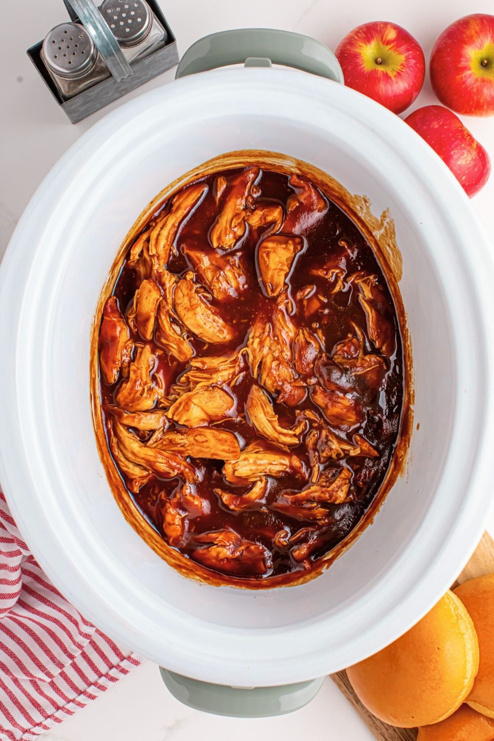 overhead look of crockpot on table full of Crockpot Apple Butter BBQ Pulled Chicken with apples on table to side of container